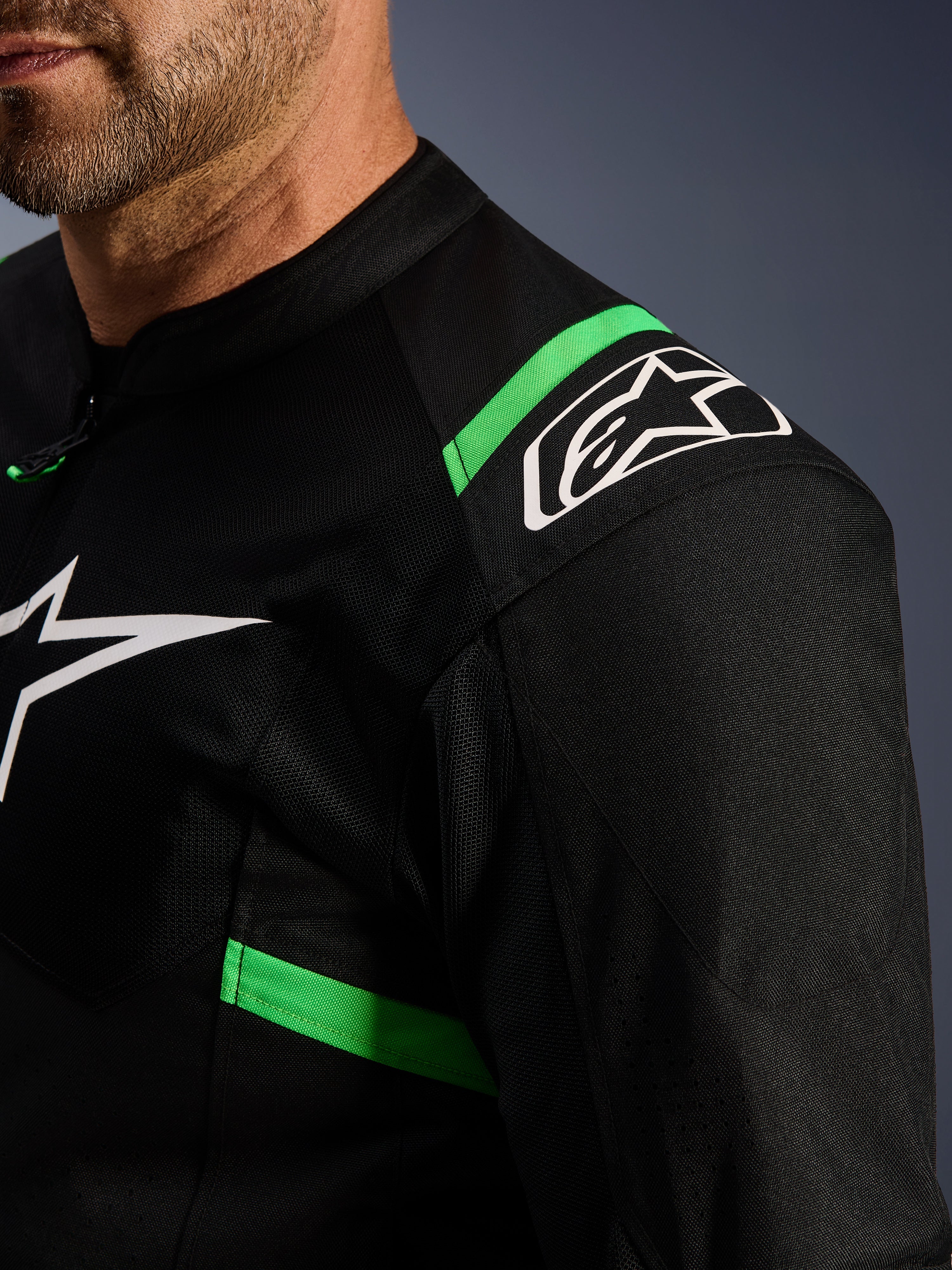 Alpinestars T-SPS Air V2 Jas, zwart en fluo groen, close-up van schouder en borst, wit Alpinestars ster-logo, technisch mesh-materiaal voor luchtstroom, sportieve motorjas