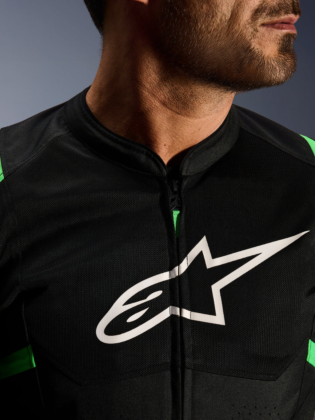 Close-up van Alpinestars T-SPS Air V2 Jacket, zwart en fluo groen, voorzien van ademende tech mesh panelen, centrale ritssluiting en een prominent wit Alpinestars sterlogo op de borst, performance motorkleding