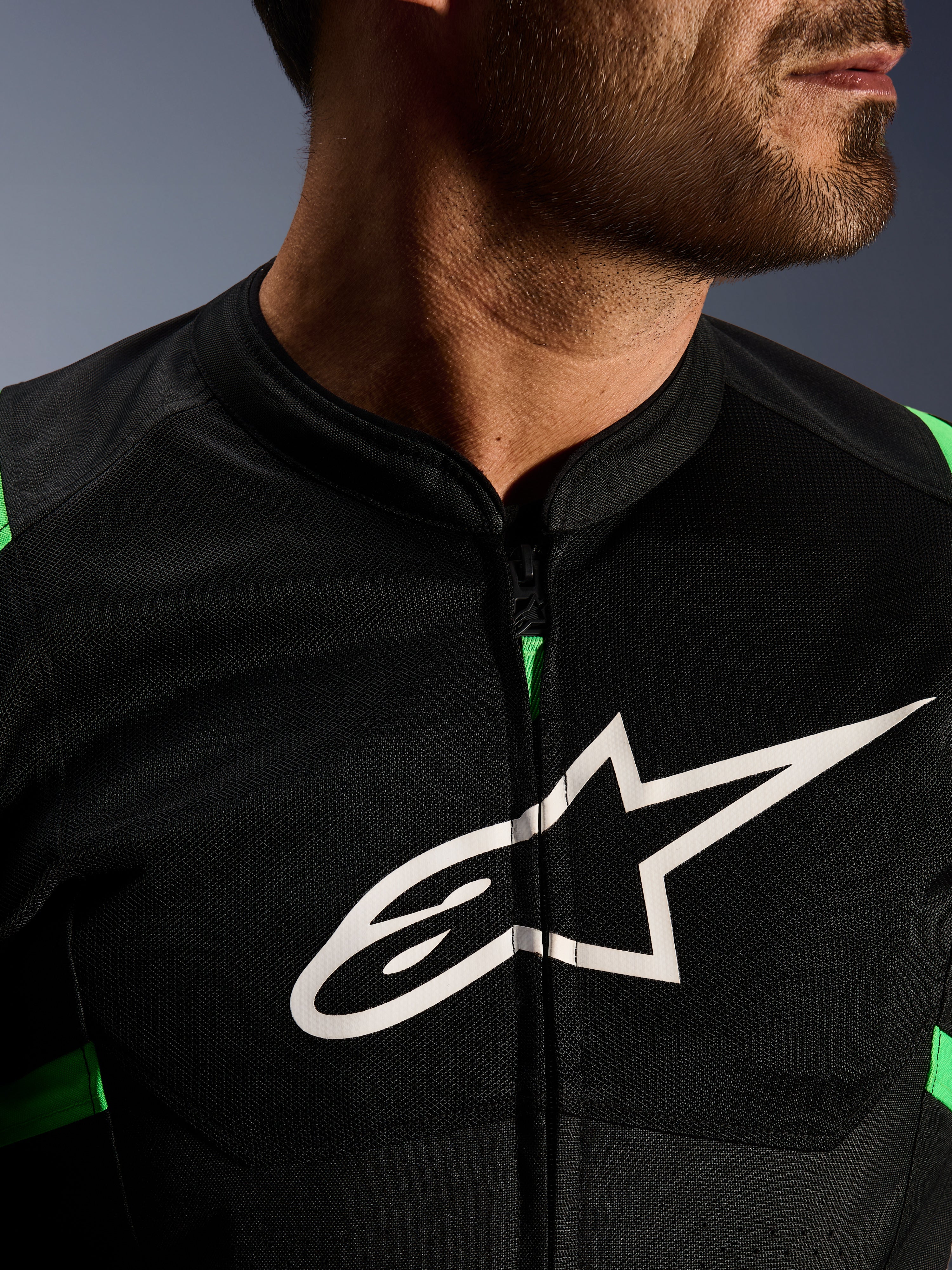 Close-up van Alpinestars T-SPS Air V2 Jacket, zwart en fluo groen, voorzien van ademende tech mesh panelen, centrale ritssluiting en een prominent wit Alpinestars sterlogo op de borst, performance motorkleding