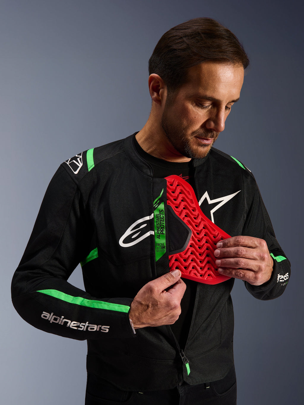Alpinestars T-SPS Air V2 Jas, motorjas in zwart en fluogroen, man demonstreert rode Nucleon borstprotector insert, Tech-Air Ready label, sportief textielontwerp met mesh panelen
