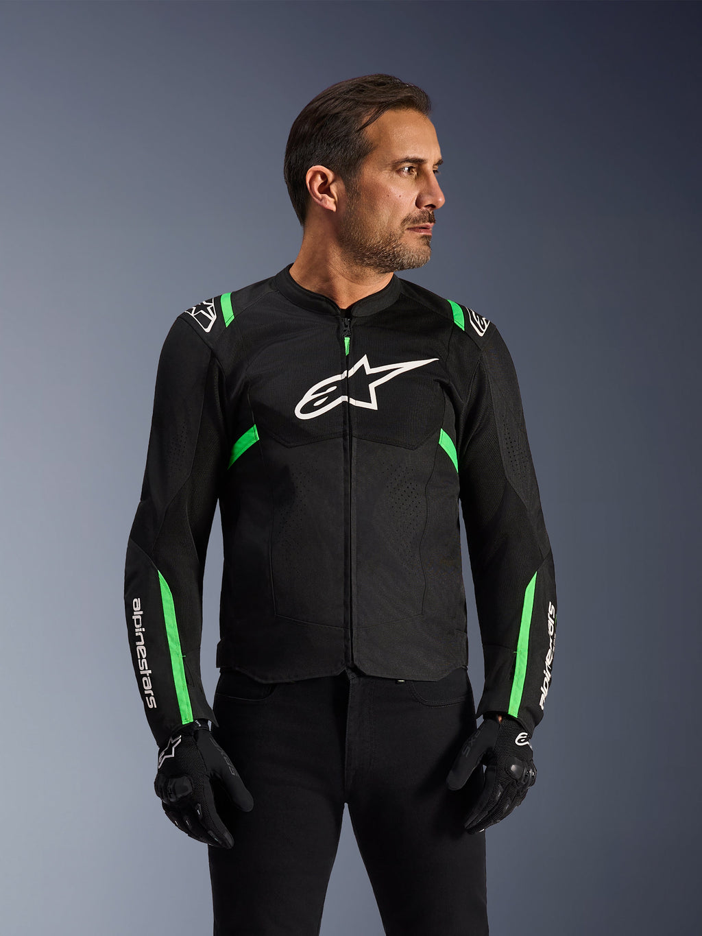 Alpinestars T-SPS Air V2 jas, motorjas, zwart met fluogroen, gedragen door een model met zwarte motorhandschoenen en broek, met wit Alpinestars-logo op de borst en neongroene accenten op de schouders en mouwen, tech mesh-panelen voor ventilatie, sportieve pasvorm voor stedelijk rijden