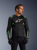 Alpinestars T-SPS Air V2 jas, motorjas, zwart met fluogroen, gedragen door een model met zwarte motorhandschoenen en broek, met wit Alpinestars-logo op de borst en neongroene accenten op de schouders en mouwen, tech mesh-panelen voor ventilatie, sportieve pasvorm voor stedelijk rijden