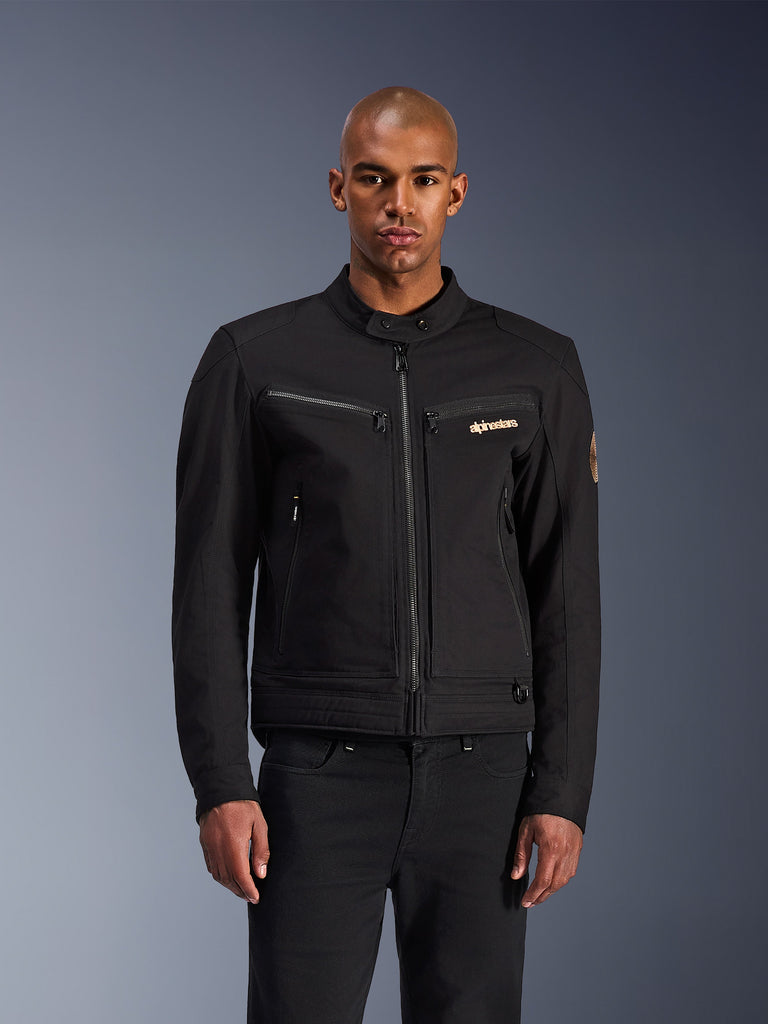 Alpinestars Bruiser Jacket, zwarte motorjas, hoge kraag met knoop, ritssluiting vooraan, logo op borst, ritszakken, strakke moderne pasvorm