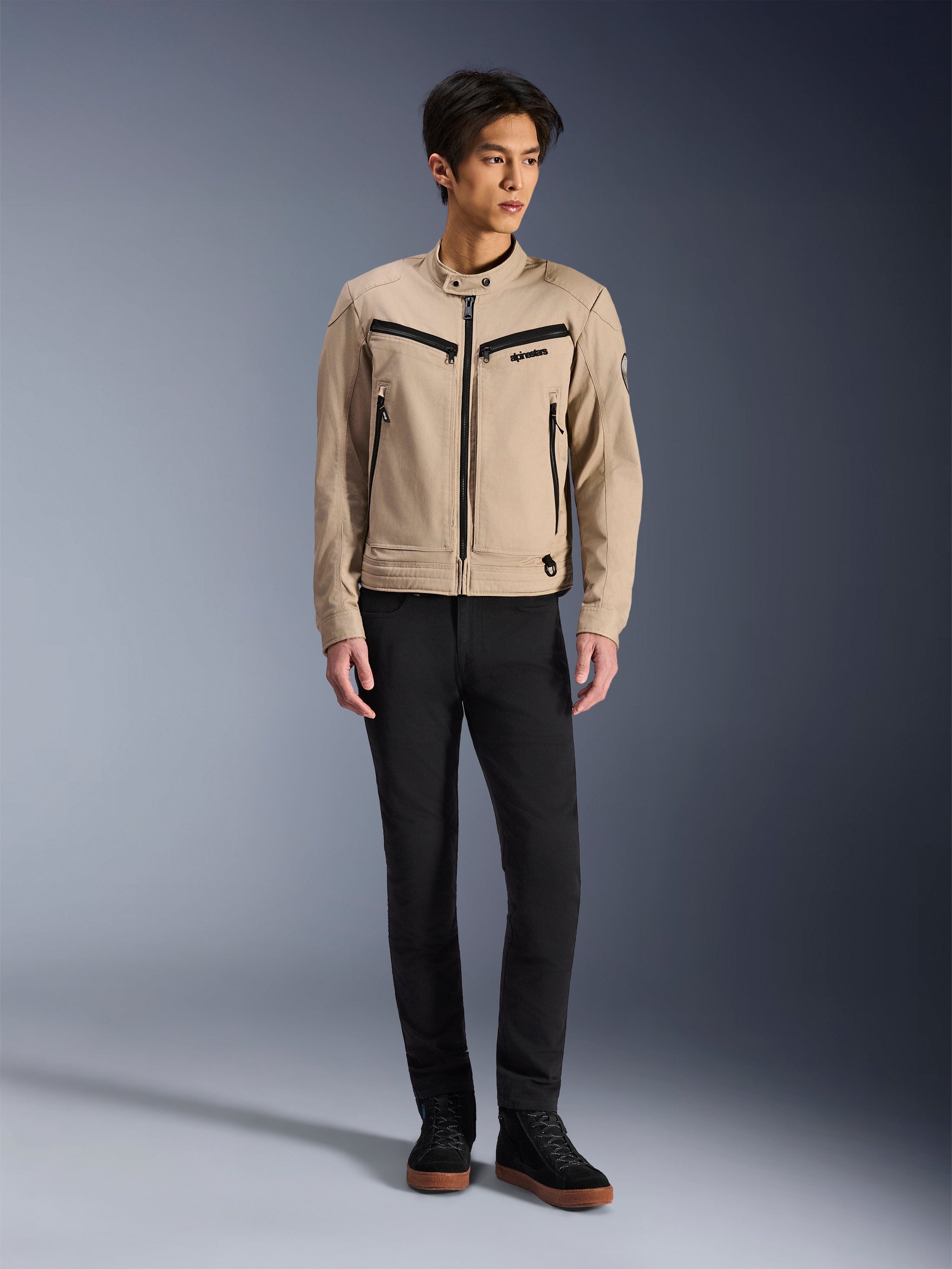 Alpinestars Bruiser Jacket, Urban Motorcycle Jacket in Aluminum, worn with black pants and black sneakers, featuring black zippered pockets and a snap collar, contemporary workwear-inspired design for urban riding