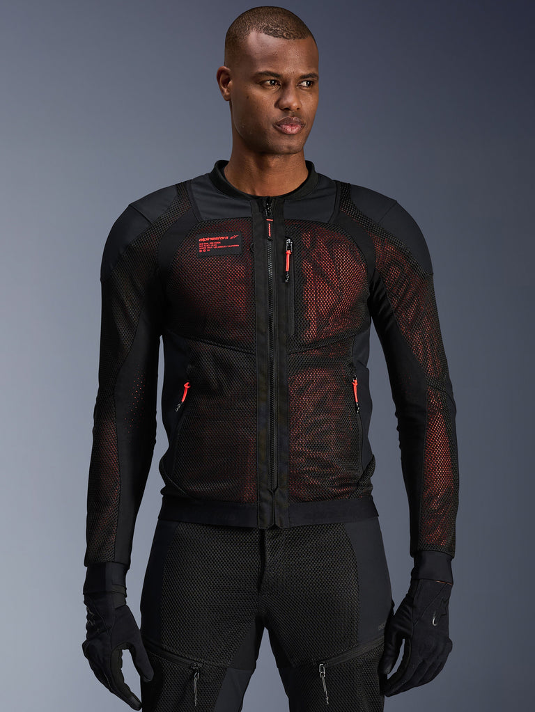 Alpinestars Troop-Air Pro Jacket, technische gepantserde mesh motorjas in Black Red Fluo, gedragen door een model, voorzien van grote mesh ventilatiepanelen, rode onderlaag en rode ritstrekkers, urban rijstijl.