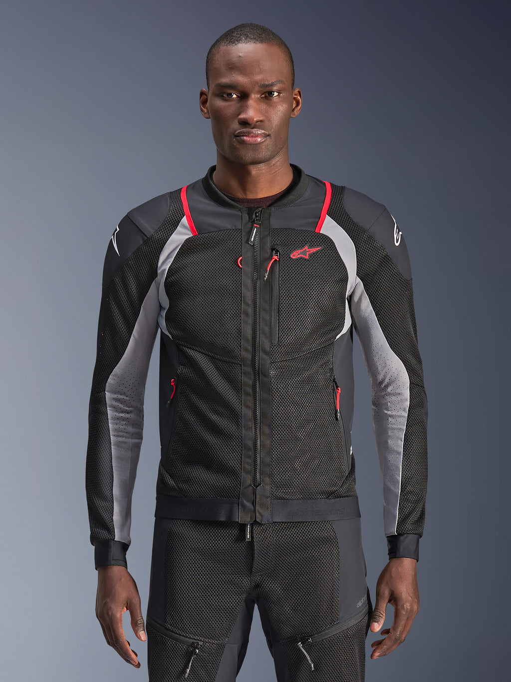 Alpinestars Troop-Air Pro Jacket, zwart, asgrijs en felrood, gedragen door een model, motorjas van mesh met geperforeerde ventilatiepanelen, voorzien van rode zakken met rits en witte logo's op de schouders, technische motoruitrusting met protectie