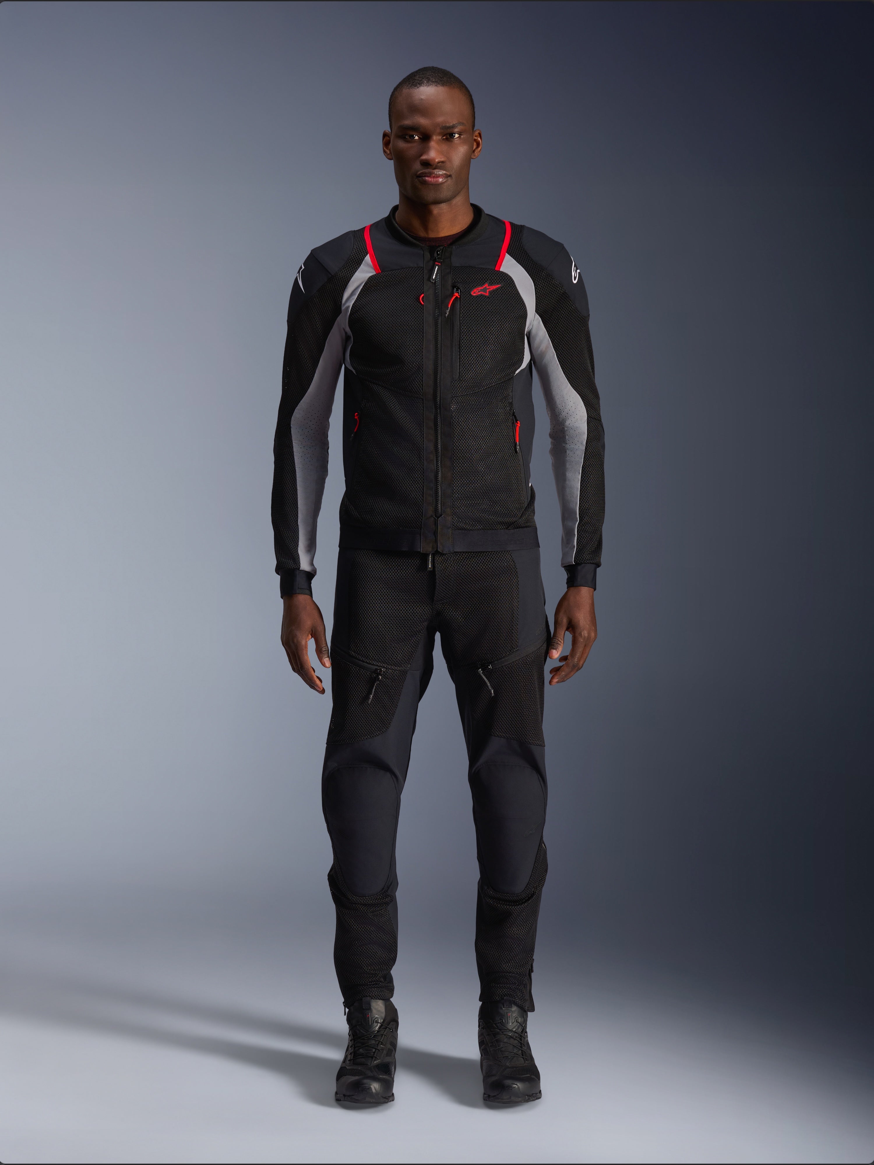 Alpinestars Troop-Air Pro Jas, technische motorjas, Black Ash Gray en Bright Red, voorzien van mesh-panelen en rode accenten, gedragen door mannelijk model met zwarte motorbroek en laarzen, strak urban ontwerp met technische ventilatie.