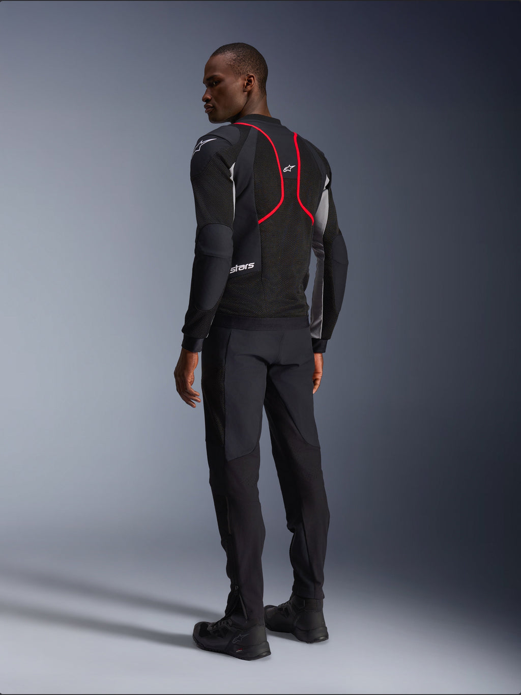 Alpinestars Troop-Air Pro Jas, motorjas, zwart, asgrijs en felrood, achteraanzicht op model, met rode accentlijnen en mesh ventilatiepanelen, gedragen met zwarte broek en laarzen, urbane motorstijl