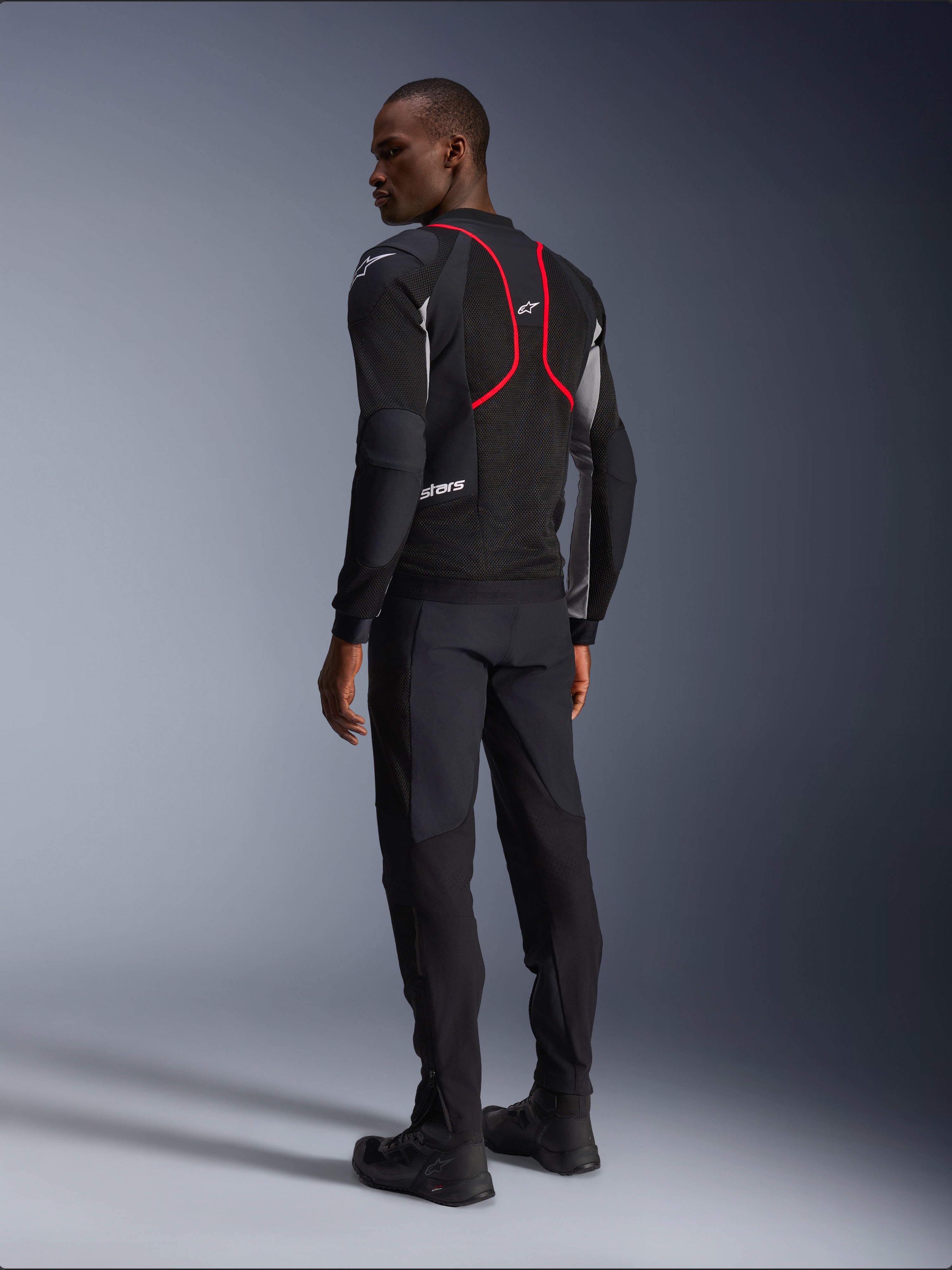Alpinestars Troop-Air Pro Jas, motorjas, zwart, asgrijs en felrood, achteraanzicht op model, met rode accentlijnen en mesh ventilatiepanelen, gedragen met zwarte broek en laarzen, urbane motorstijl