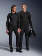 Alpinestars Stella Troop-Air jas, man en vrouw in bijpassende volledig zwarte technische motoruitrusting, voorzien van mesh-constructie voor luchtstroom, zwarte broek en laarzen, man houdt een zwarte helm vast, urban motorkleding