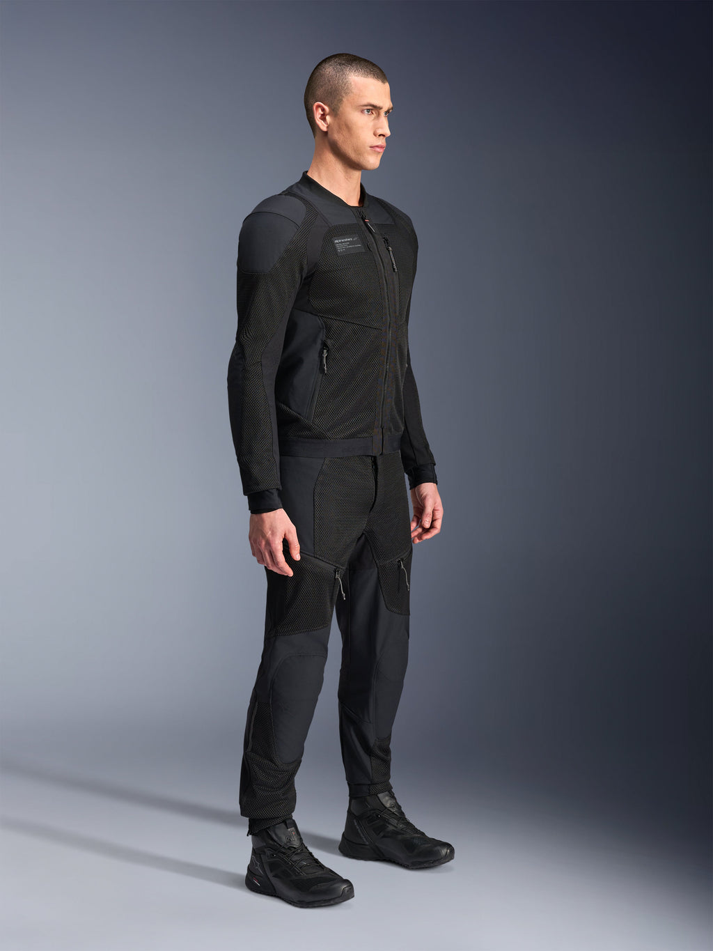 Alpinestars Troop-Air Pro Jas, technische gepantserde doorwaaijas, zwart, gedragen door een model met bijpassende zwarte motorbroek en laarzen, voorzien van een geavanceerde 2D tech mesh-structuur en ademende ventilatiepanelen, urban contemporary motorkleding.