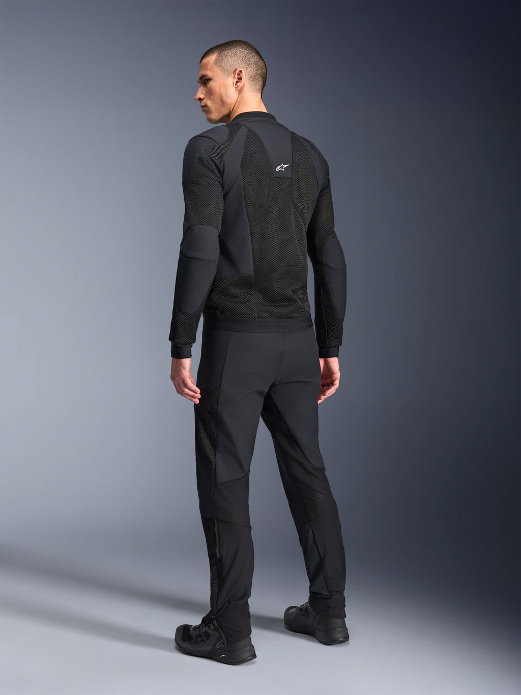 Alpinestars Troop-Air Pro Jacket, zwart, technische gepantserde luchtjas van de achterkant getoond, voorzien van uitgebreide mesh-panelen voor luchtstroom, gecombineerd met bijpassende zwarte technische broek en schoenen.