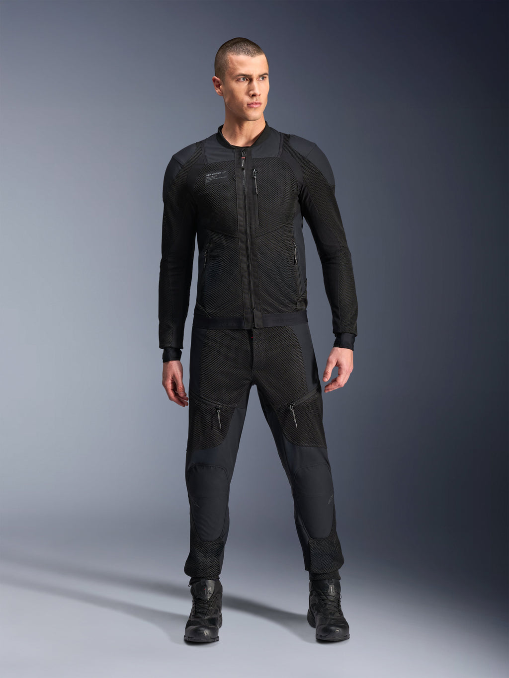 Alpinestars Troop-Air Pro Jas, zwarte technische gepantserde motorjas, voorzien van mesh-panelen en ritsen aan de voorkant, gedragen met bijpassende zwarte broek en motorlaarzen, premium urban road gear