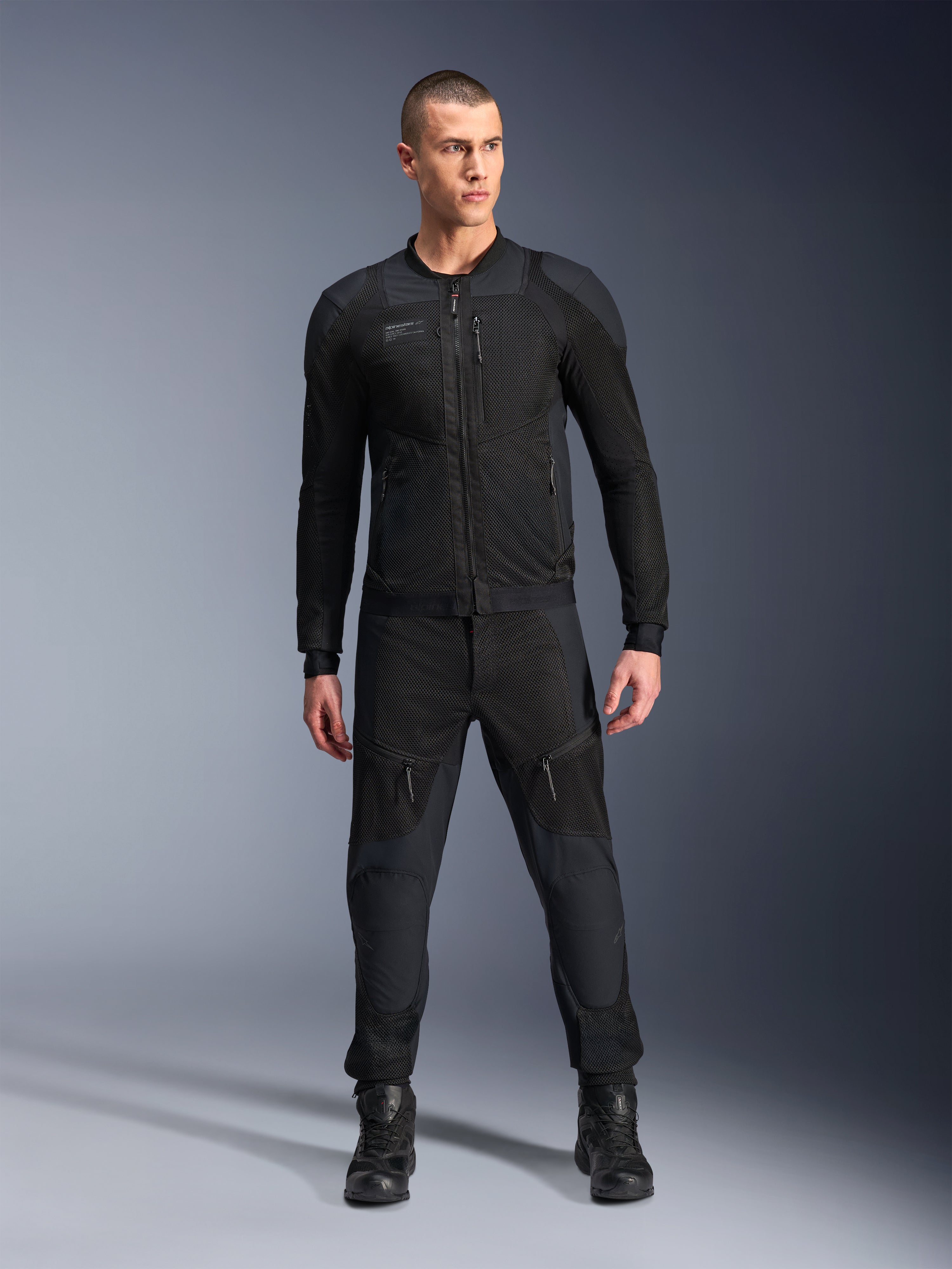 Alpinestars Troop-Air Pro Jas, zwarte technische gepantserde motorjas, voorzien van mesh-panelen en ritsen aan de voorkant, gedragen met bijpassende zwarte broek en motorlaarzen, premium urban road gear
