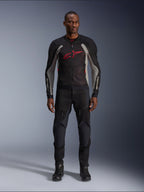 Mannelijk model draagt de Alpinestars Troop-Air Jas in Black Ash Gray en Bright Red, technische mesh motorjas met een opvallend rood logo op de borst, gecombineerd met een zwarte motorbroek en laarzen, stedelijke motorkleding