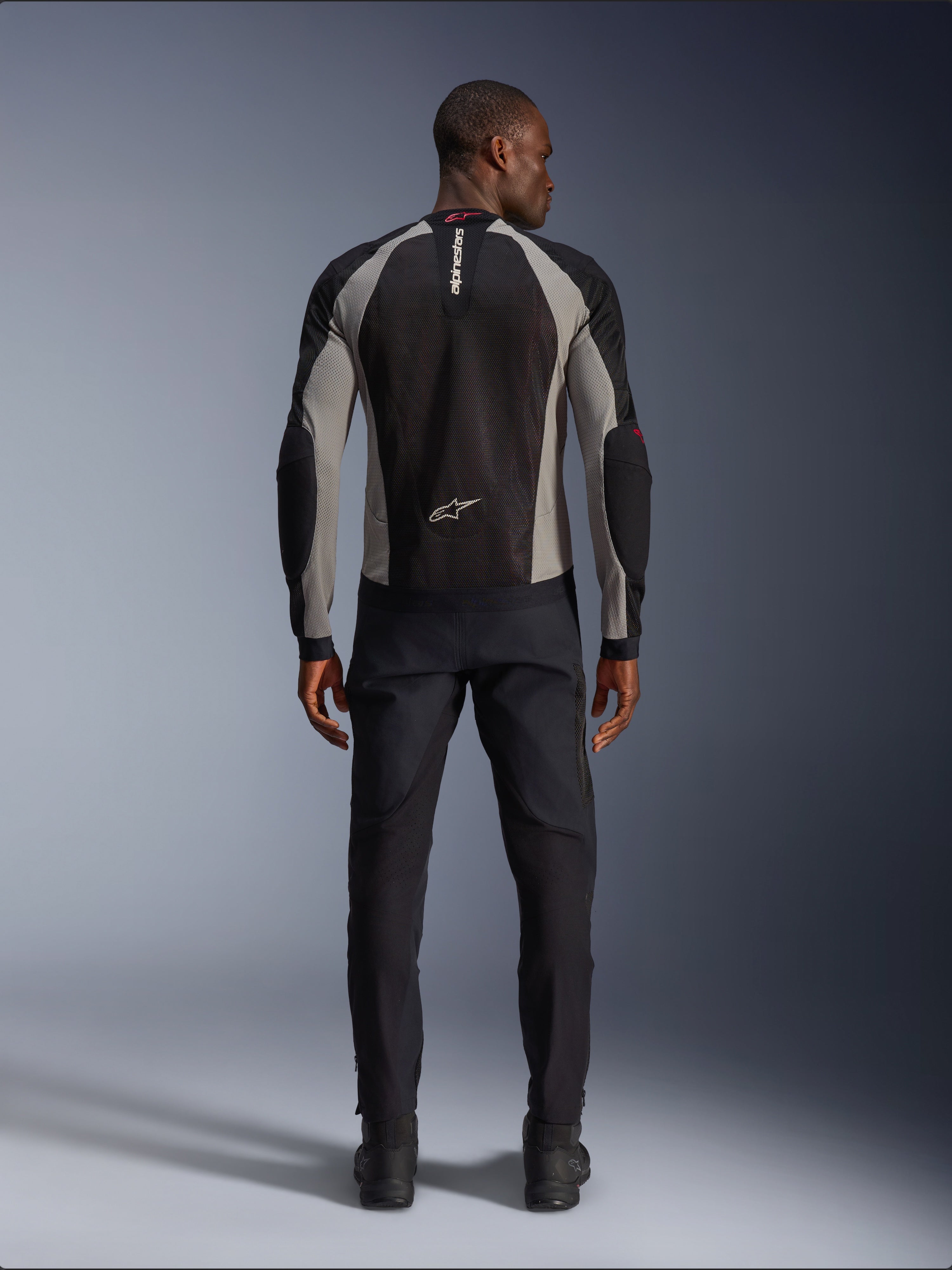 Alpinestars Troop-Air Jas, motorjas in Black Ash Gray en Bright Red, achteraanzicht op mannelijk model, lichtgewicht mesh-constructie voor ventilatie, Alpinestars-logo op de kraag en onderrug, gecombineerd met een zwarte motorbroek