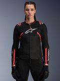 Alpinestars Woman Stella T-Sps Air V2 Jacket, textiele motorjas, zwart met Diva Pink accenten, ademende mesh-panelen en roze details, wit Alpinestars-logo op de borst, vrouwelijk model draagt zwarte motorbroek en handschoenen