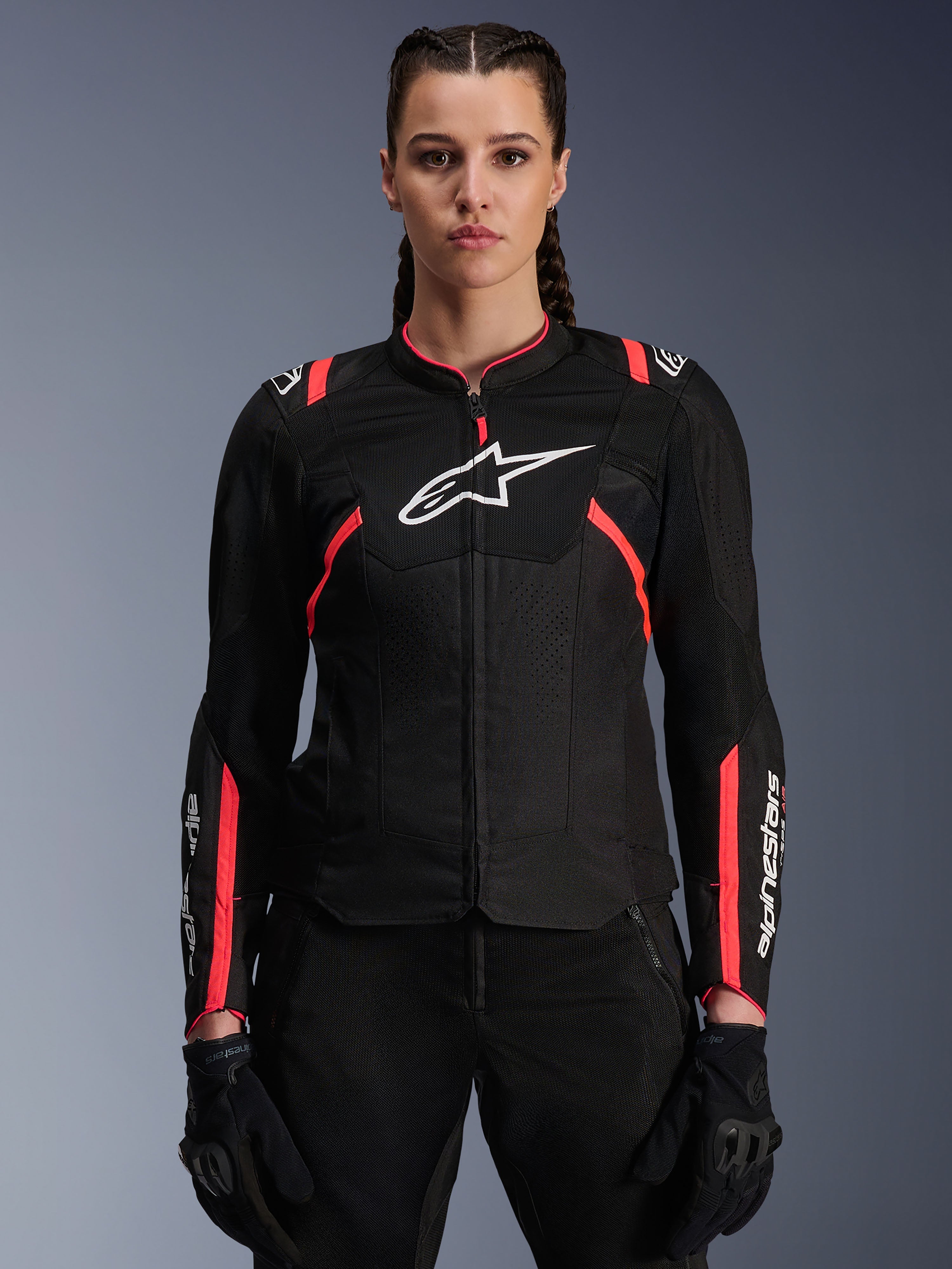 Alpinestars Woman Stella T-Sps Air V2 Jacket, textiele motorjas, zwart met Diva Pink accenten, ademende mesh-panelen en roze details, wit Alpinestars-logo op de borst, vrouwelijk model draagt zwarte motorbroek en handschoenen