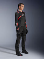 Vrouwelijke motorrijder die de Alpinestars Stella T-SPS Air V2-jas draagt in zwart en Diva Pink, dames motorjas van textiel met mesh-panelen en roze accenten, gecombineerd met een zwarte motorbroek en handschoenen, volledige studio-opname.