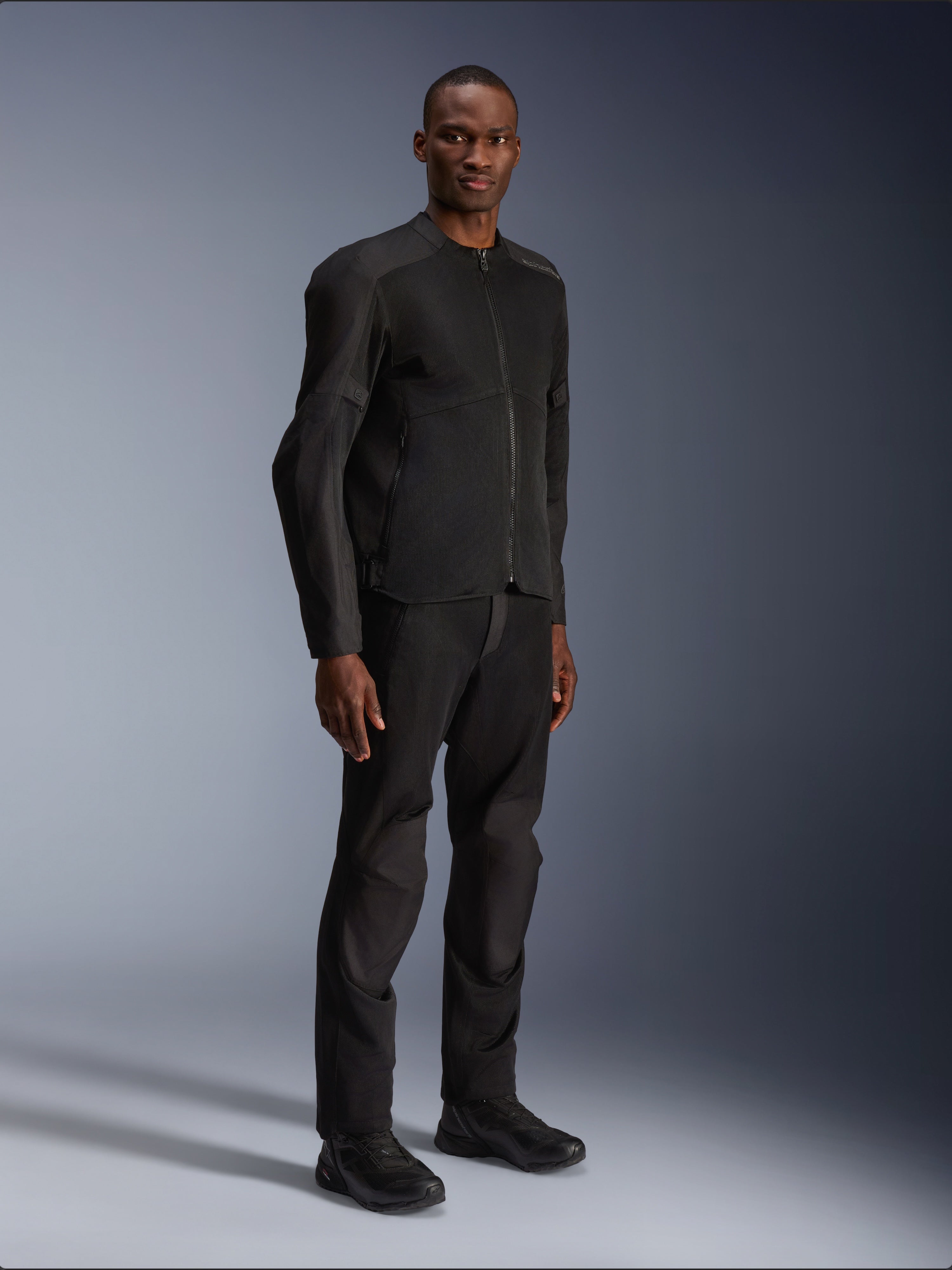 Alpinestars C-1 Air Jacket, zwart, gedragen door een model met bijpassende zwarte motorbroek en schoenen, voorzien van grote tech mesh panelen voor luchtstroom, strakke urban esthetiek met een gestroomlijnde pasvorm