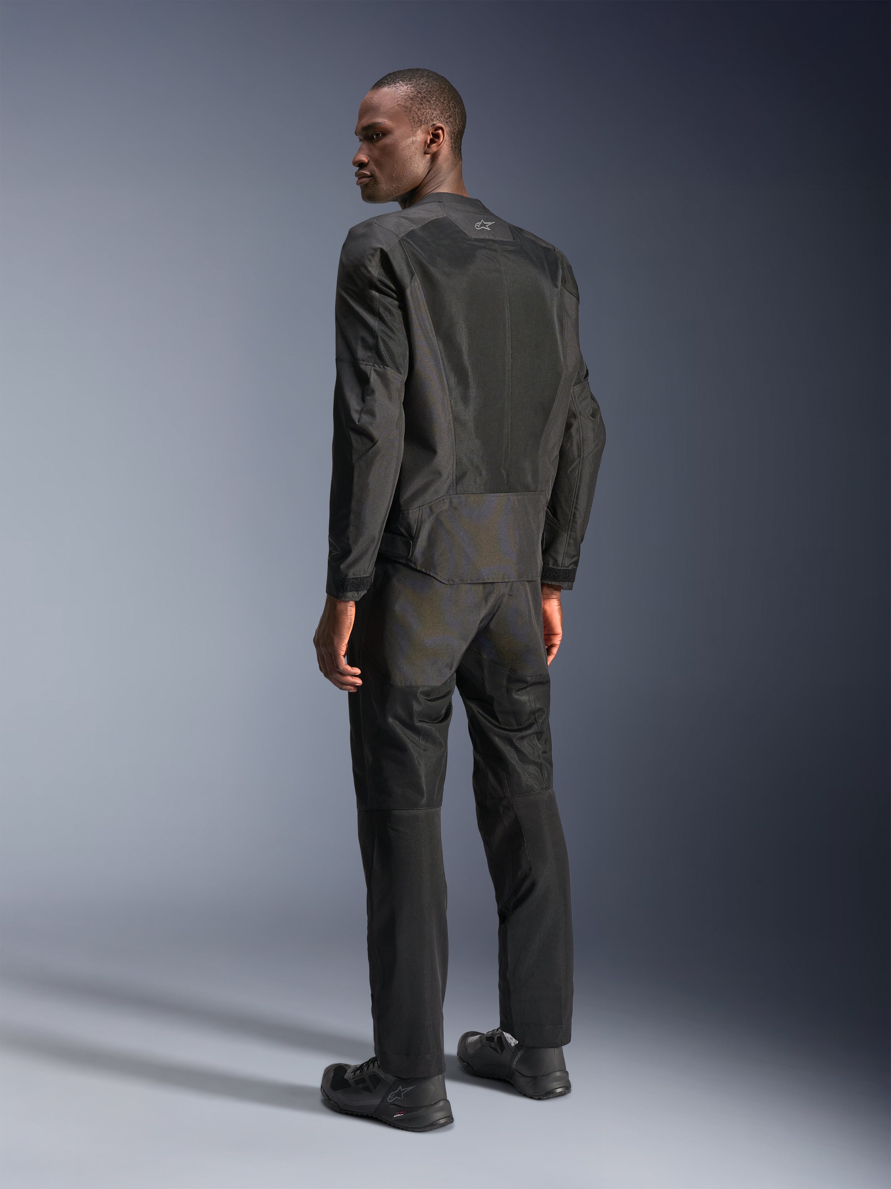 Alpinestars C-1 Air Jas, urban motorjas, zwart, achteraanzicht met tech mesh-panelen voor luchtstroom en reflecterend logo, gedragen met bijpassende zwarte motorbroek en schoenen, strakke en verfijnde esthetiek voor woon-werkverkeer in de stad