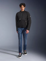 Mannelijk model draagt het zwarte Alpinestars Provoke Jacket, een urban textiele motorjas met technische ritsen en ripstop softshell-panelen, gecombineerd met een blauwe jeans en zwarte sneakers, eigentijdse urban rijderstijl.