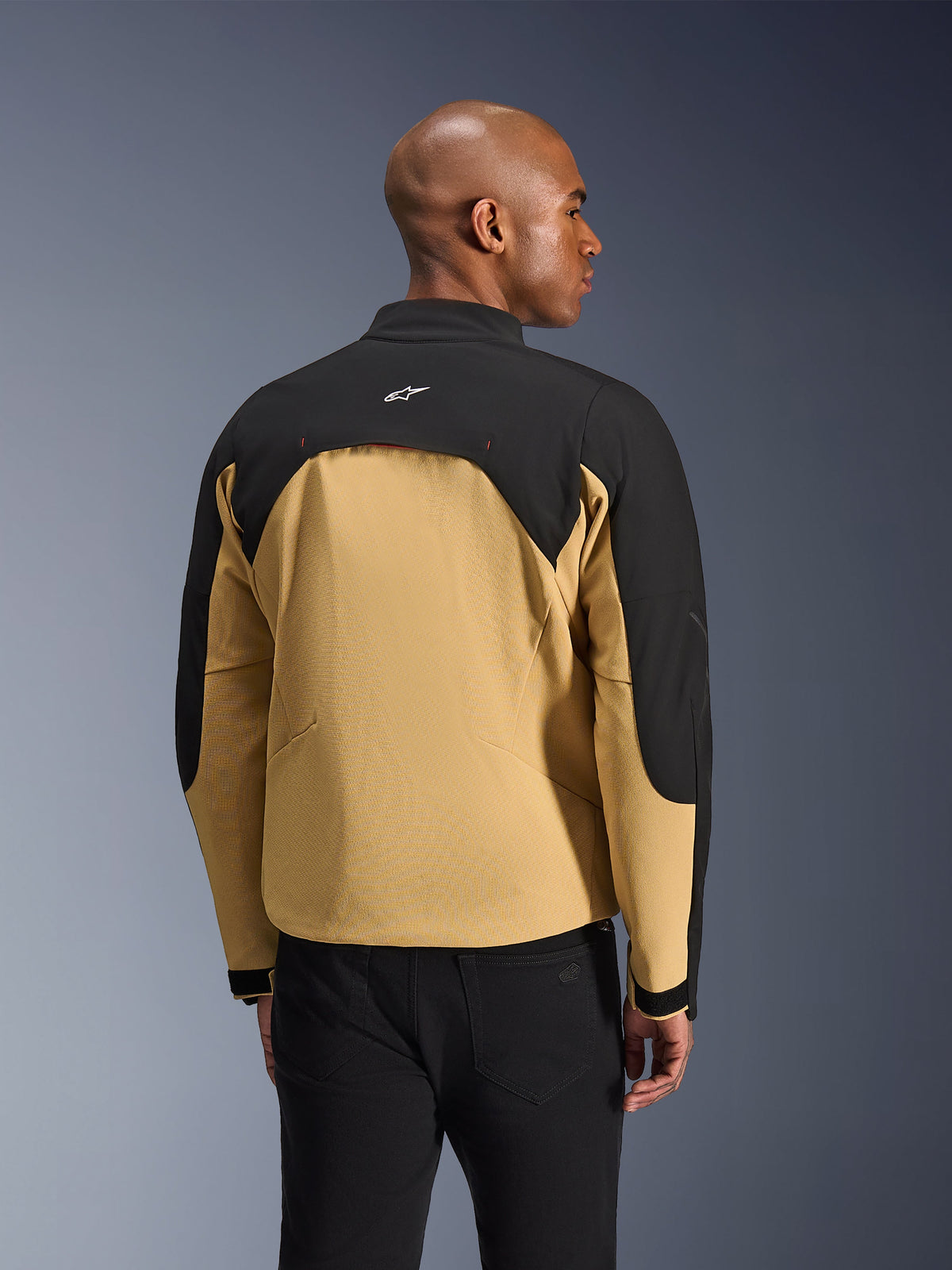 Alpinestars Provoke Jacket, urbane motorjas, zwart en camel, achteraanzicht met tweekleurige constructie, met mesh gevoerd ventilatiepaneel op de rug, klein wit logo op de bovenrug, gedragen met zwarte broek