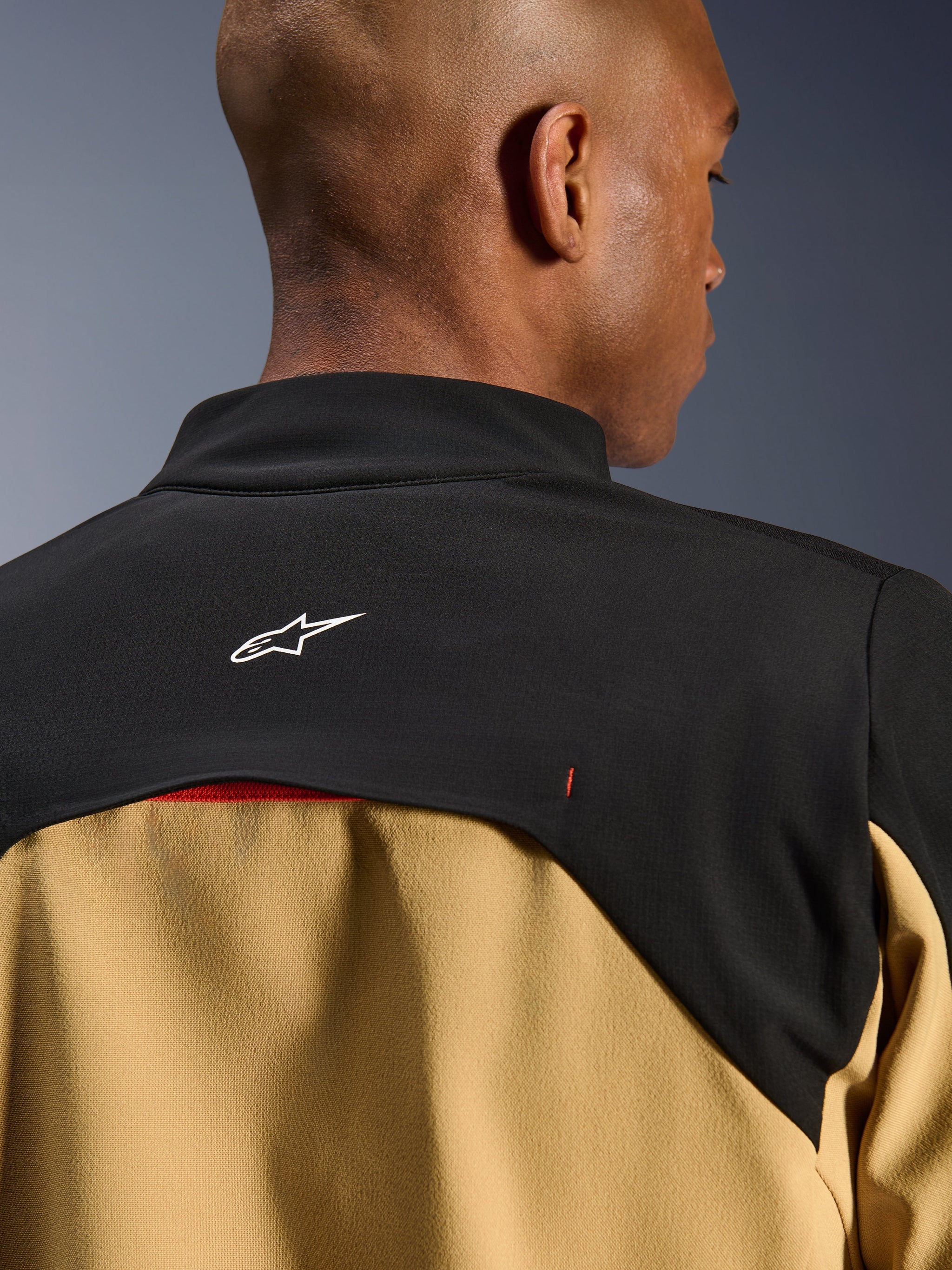 Alpinestars Provoke jas, urban motorjas, zwart en camel, close-up van de bovenrug en kraag met een wit Astars-logo op een zwart schouderstuk en camelkleurige panelen aan de onderzijde, eigentijds outdoor-geïnspireerd technisch ontwerp