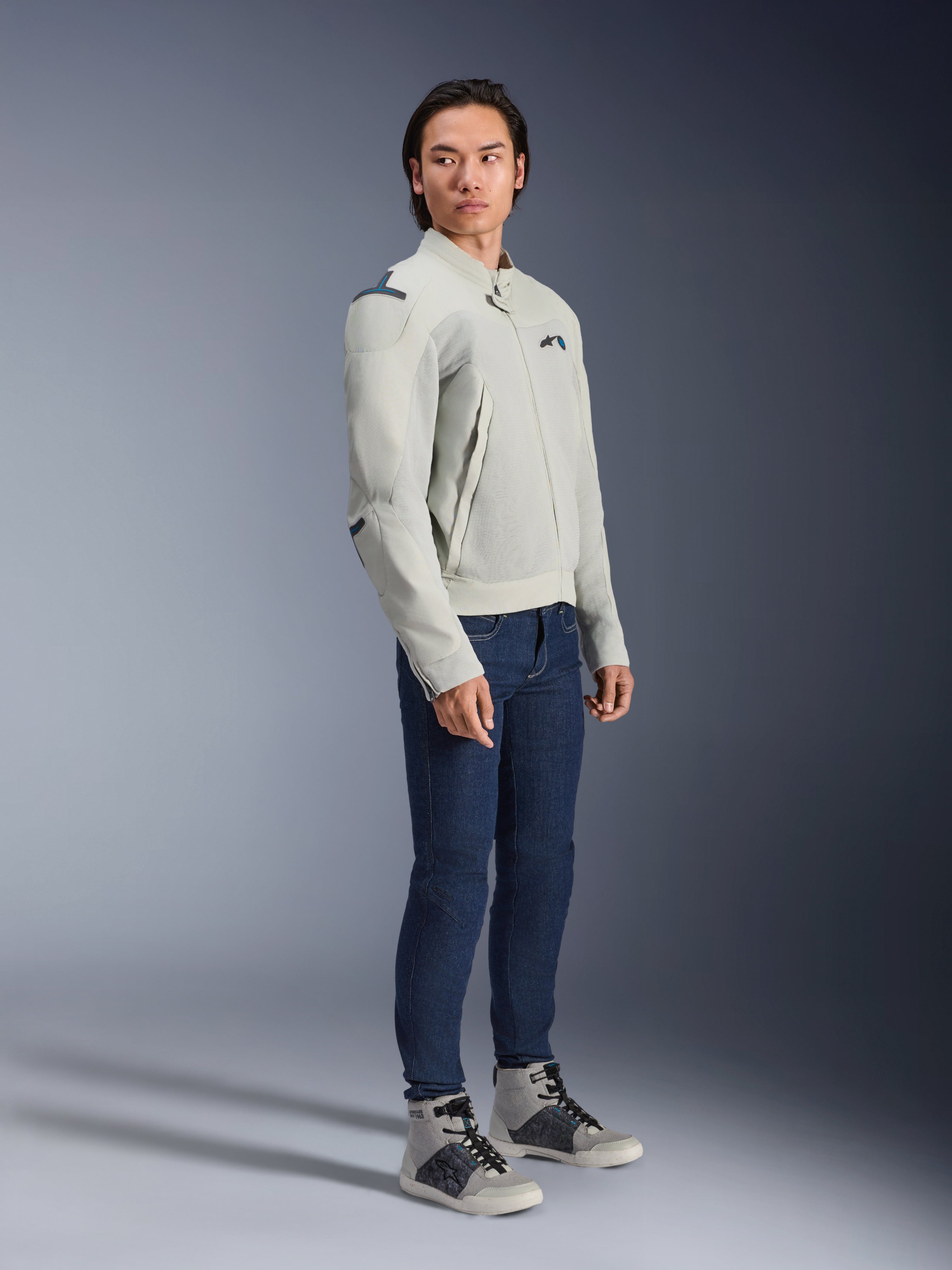 Alpinestars Circal-1 Air Jacket in Metal Gray en Methyl Blue, gedragen door een model met donkerblauwe jeans en grijze sneakers, stedelijke zomer motorjas met grote mesh ventilatiepanelen en een minimalistisch ontwerp.