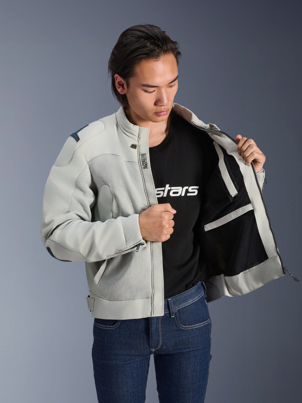 Alpinestars Circal-1 Air Jacket, metaalgrijs, opengehouden om de mesh voering aan de binnenkant en zakdetails te tonen, gedragen door een model met een zwart logo T-shirt en blauwe jeans, urban motorstijl