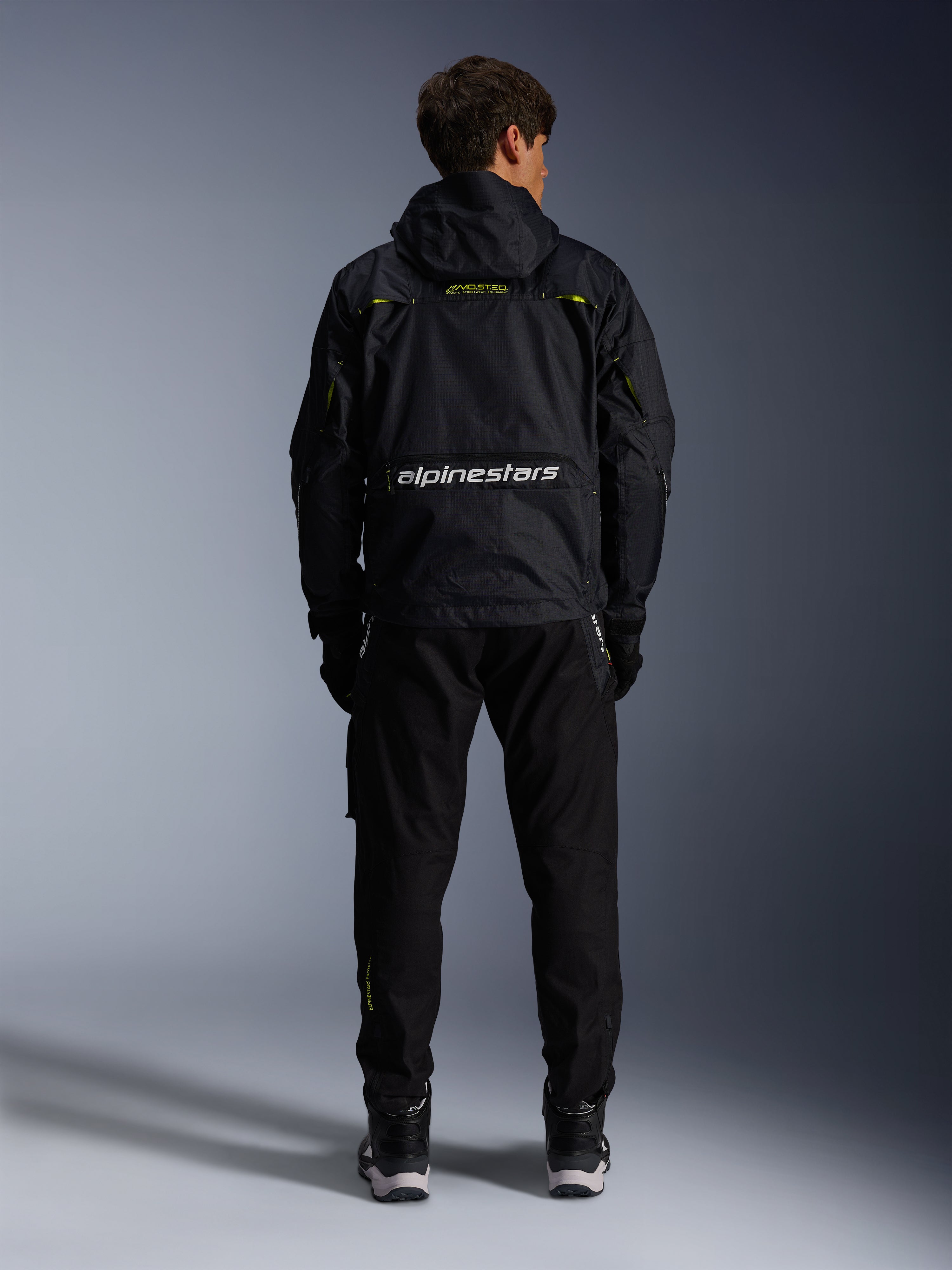 Alpinestars Mogress Air Jacket, urban motorcycle jacket, back view in black with lime punch and white accents, featuring Alpinestars branding across the lower back, worn with black pants and boots.