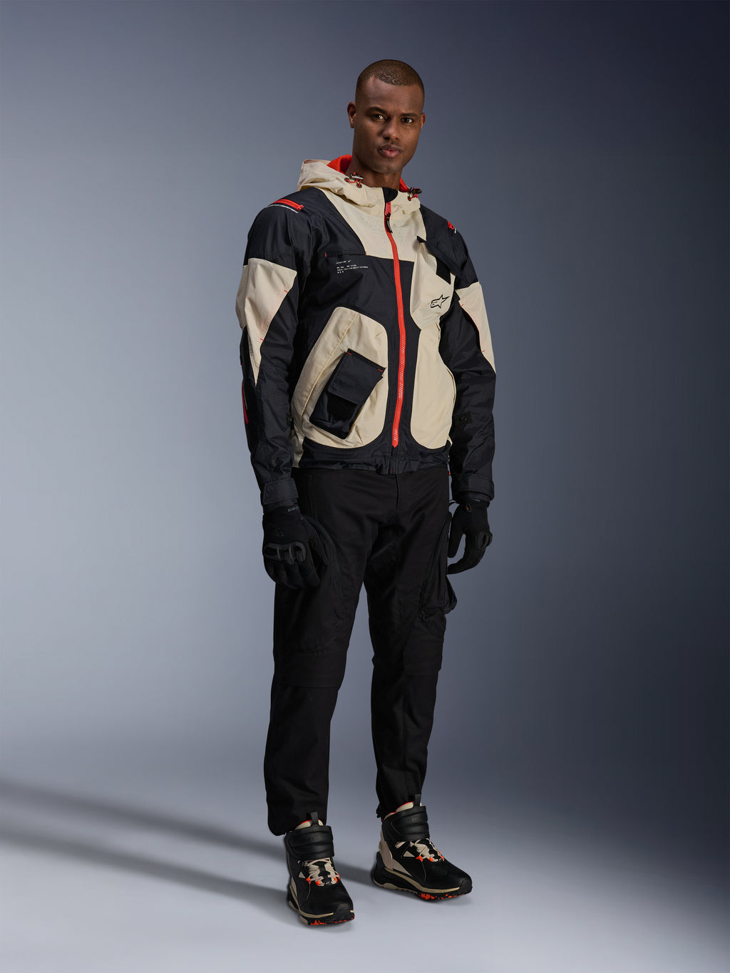 Alpinestars Acteon broek, zwarte motorbroek, gedragen met een zwart, beige en rood Mogress Air Jacket, zwarte motorhandschoenen en bijpassende hoge motorsneakers, eigentijdse urban motoruitrusting voor heren