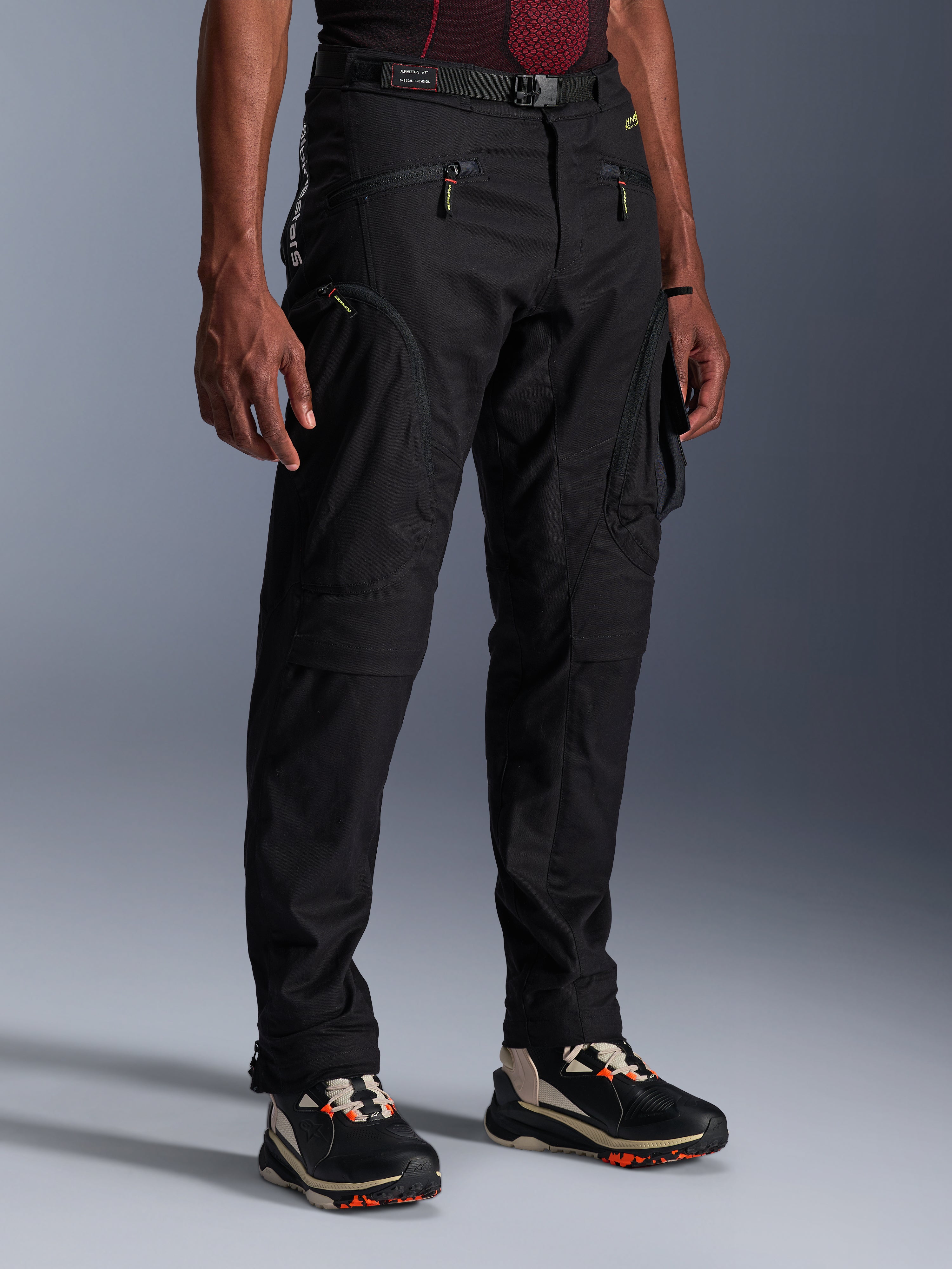 Alpinestars Acteon broek, zwarte motorbroek, gedragen door een model, met een modern taps toelopend silhouet, cargozakken met ritssluiting, verstelbare tailleriem en technische sneakers, stedelijke motorkleding