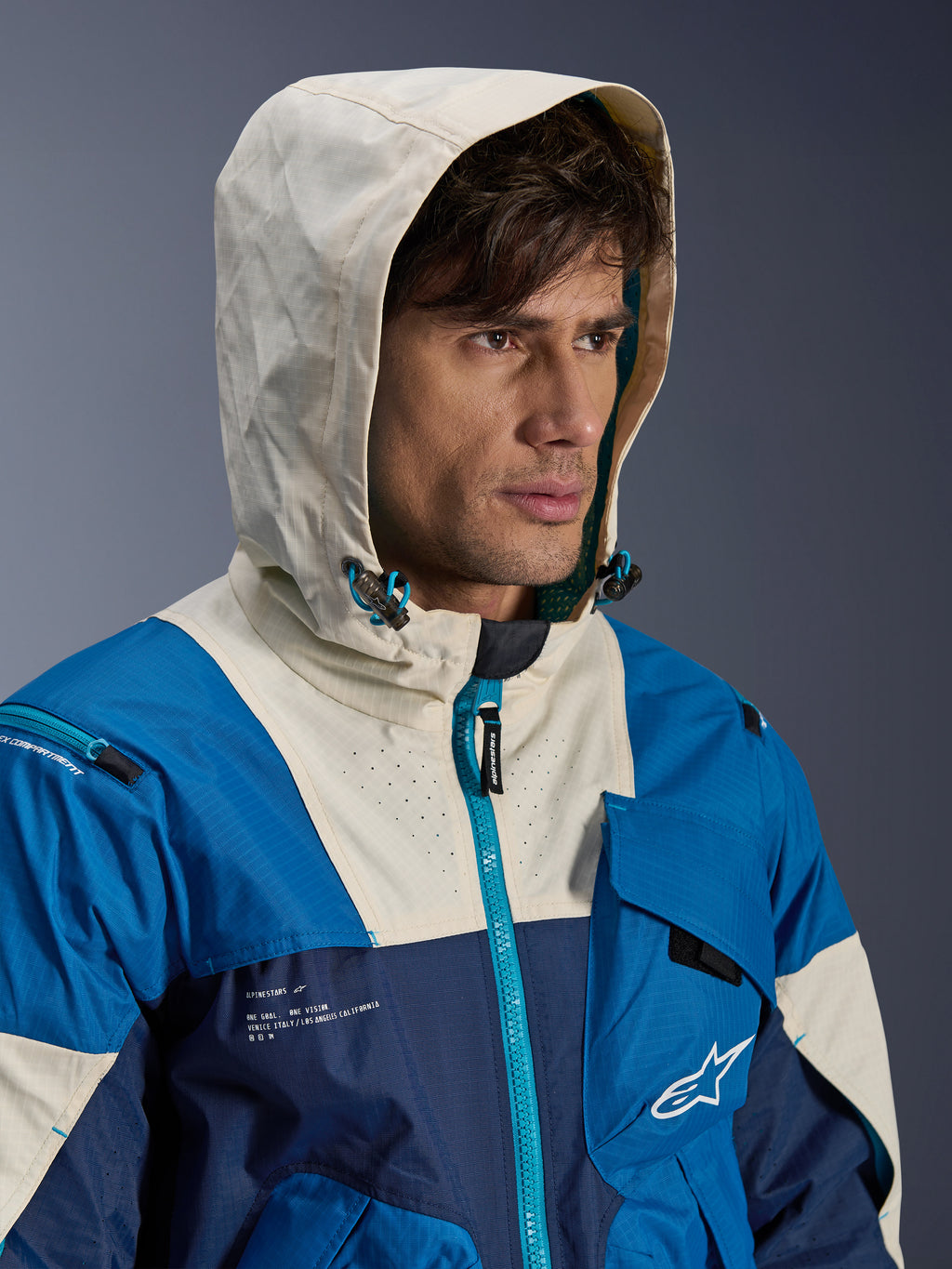 Alpinestars Mogress Air Jacket in Blue Almond, urban motorjas met een color-blocked ontwerp in blauw en crème, model draagt de capuchon op, lichtgewicht textielconstructie met technische ritsdetails.