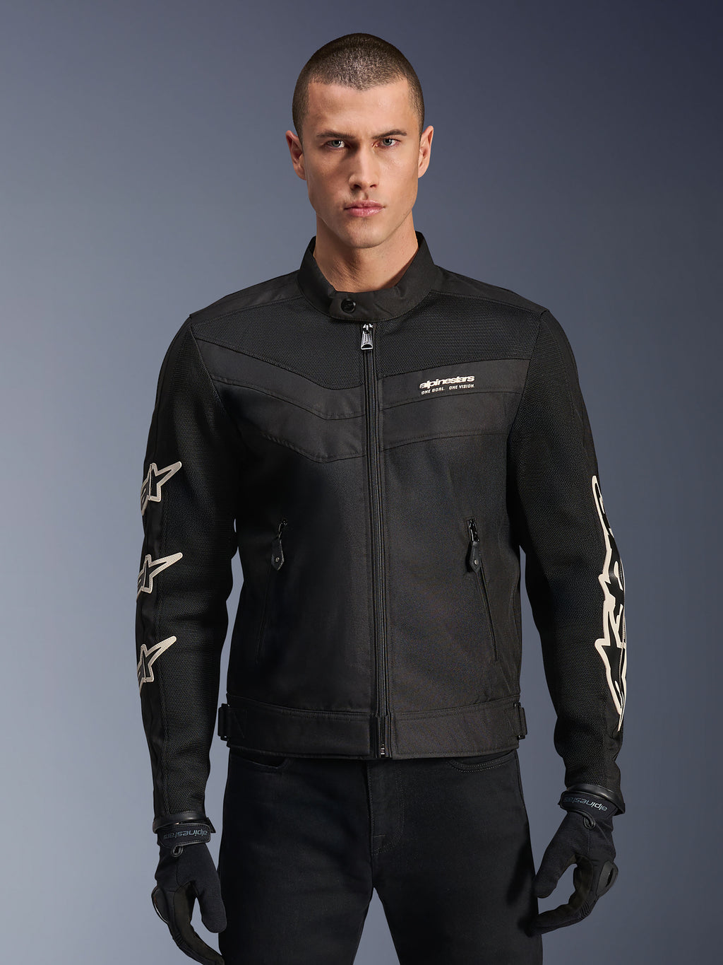 Alpinestars T-Dyno Air Jacket, zwarte textiele motorjas, voorzien van witte ster-graphics op de mouwen en logo op de borst, meshpanelen voor ventilatie, vintage-geïnspireerde biker-pasvorm, gedragen met zwarte handschoenen en broek
