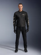 Mannelijk model in Alpinestars T-Dyno Air Jacket, zwarte lichtgewicht textiele motorjas met ademend 3D-mesh, witte sterlogo's op de mouwen, gecombineerd met zwarte broek, handschoenen en laarzen, vooraanzicht staand