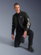 Mannelijk model draagt Alpinestars T-Dyno Air Jacket, zwarte textiele motorjas met grote witte branding op de mouwen, gecombineerd met zwarte broek en motorlaarzen, modern vintage-geïnspireerd ontwerp met 3D-meshpanelen.