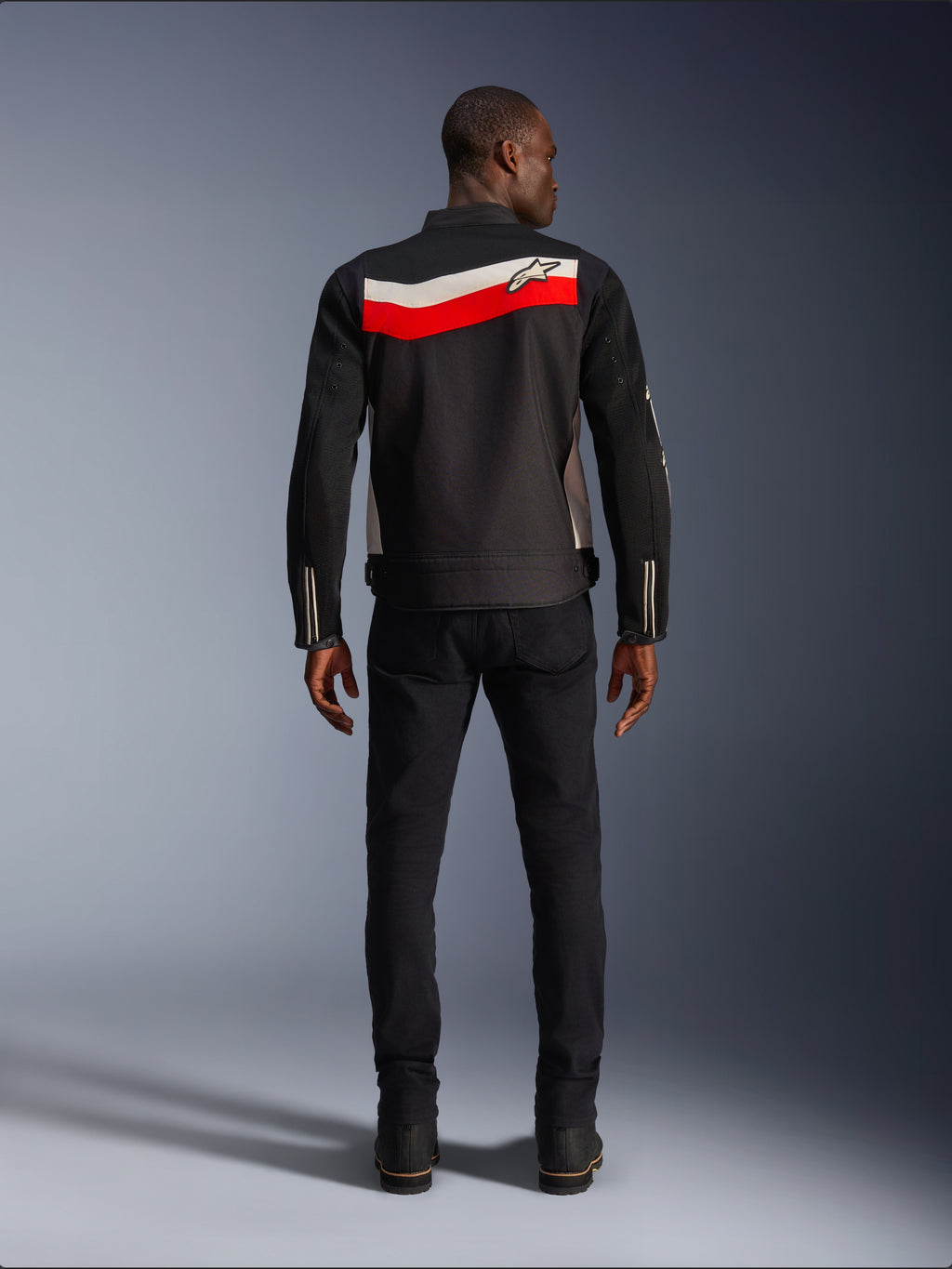 Alpinestars T-Dyno Air Jacket, textiel motorjas voor heren, achteraanzicht, zwart met felrode en ecru horizontale strepen over de rug, Alpinestars-logo op het schouderstuk, gedragen met zwarte broek en laarzen, ademende 3D mesh-constructie