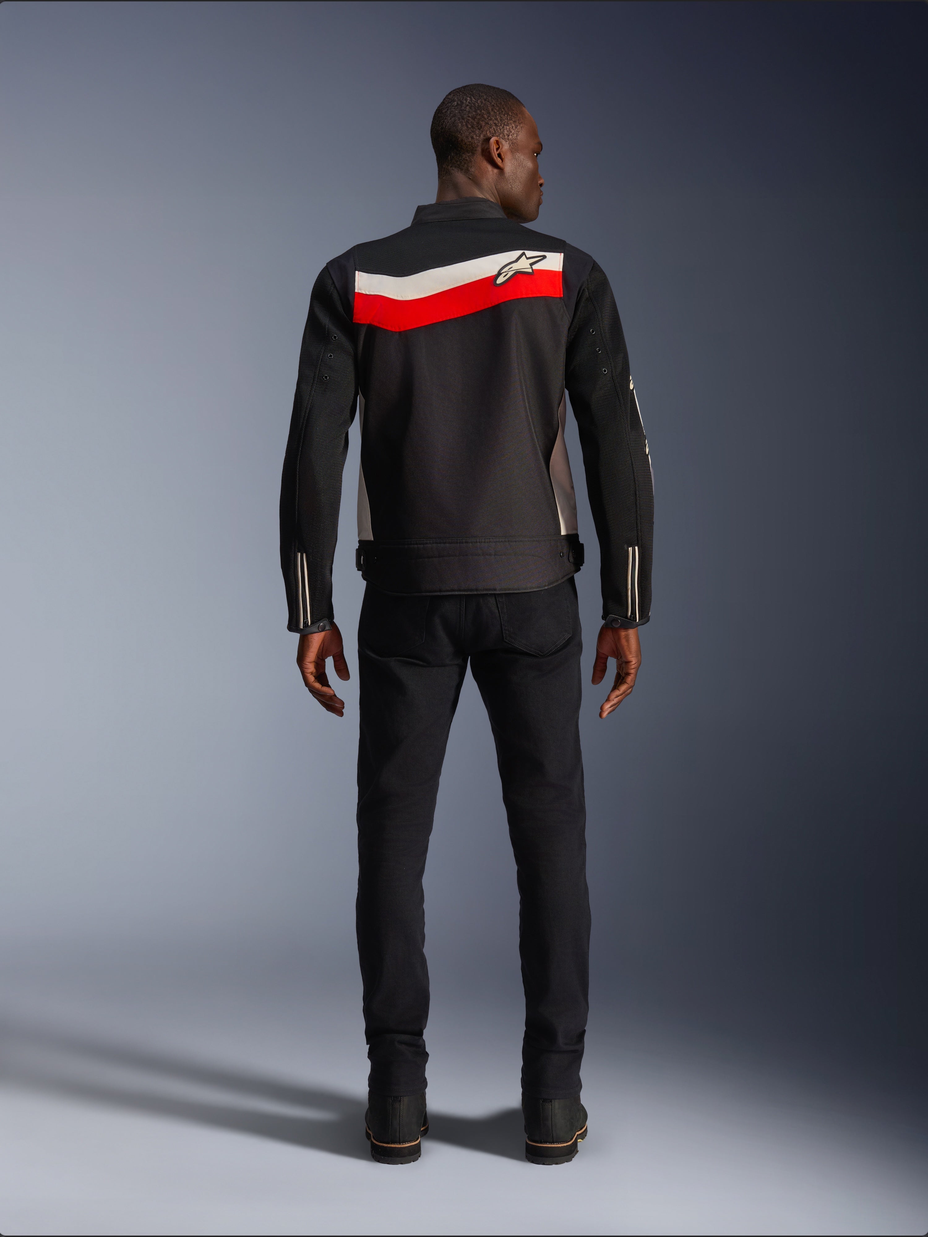 Alpinestars T-Dyno Air Jacket, textiel motorjas voor heren, achteraanzicht, zwart met felrode en ecru horizontale strepen over de rug, Alpinestars-logo op het schouderstuk, gedragen met zwarte broek en laarzen, ademende 3D mesh-constructie