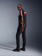 Een man die de Alpinestars T-Dyno Air Jas draagt in zwart, helderrood en ecru, vintage-geïnspireerde textiele motorjas met mesh-panelen, opvallende branding op de mouw, gecombineerd met een zwarte broek en laarzen voor een moderne biker-look