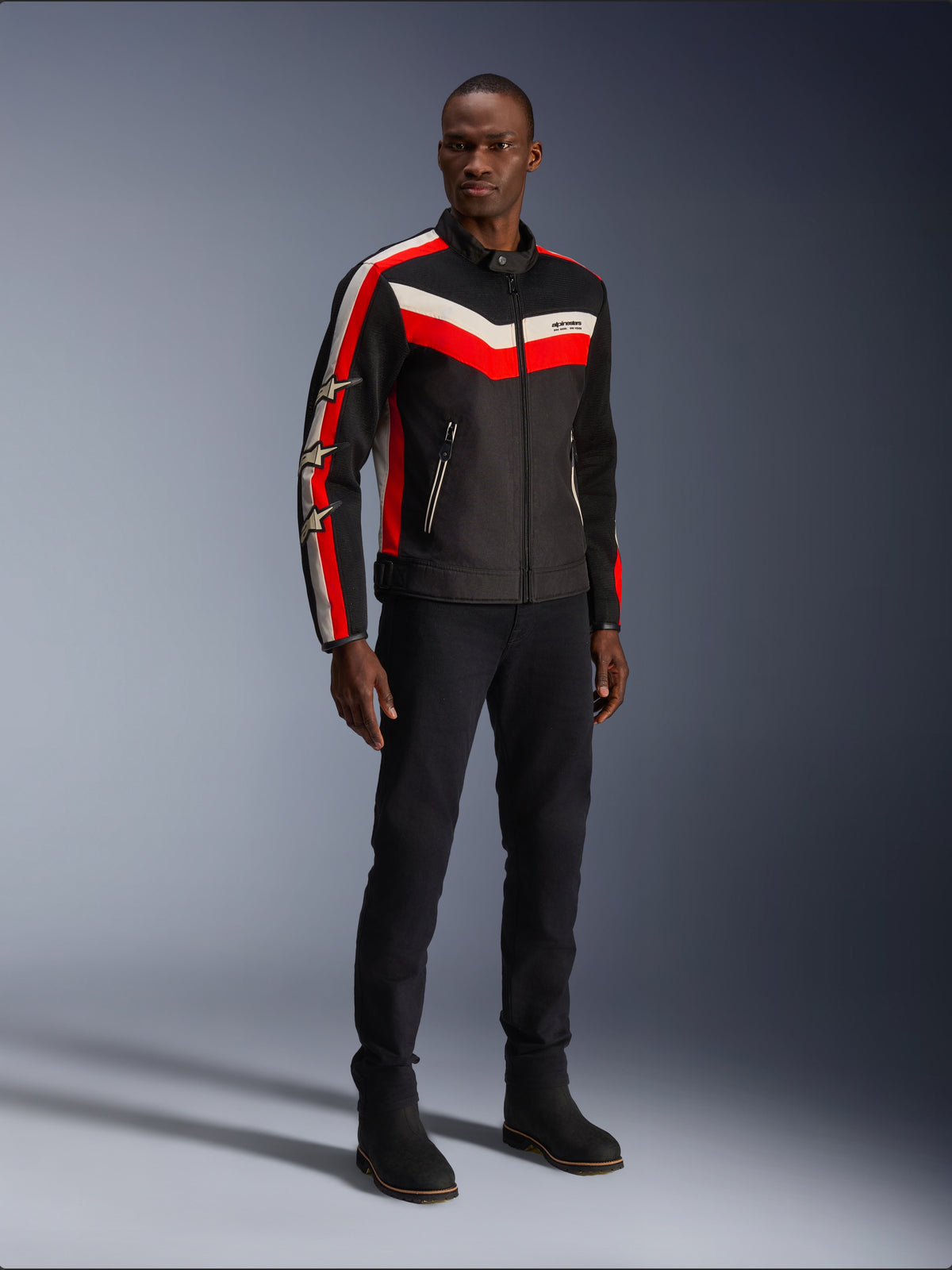 Alpinestars T-Dyno Air Jacket, Zwart Felrood Ecru, textiele motorjas voor heren met 3D-meshpanelen, rode en witte chevronstrepen op de borst en sterlogo's op de mouwen, gedragen door een model met zwarte broek en laarzen.