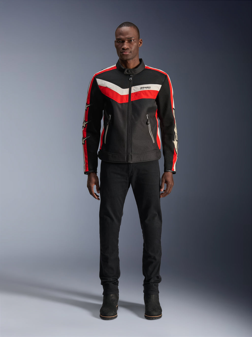 Alpinestars T-Dyno Air Jacket, textiel motorjas, zwart, helderrood en ecru, gedragen door een model met zwarte broek en laarzen, vintage-geïnspireerd ontwerp met opvallende kleurstrepen op de borst, sterlogo's op de mouwen en ademende mesh-constructie voor urban rijden.
