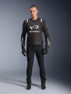 Alpinestars T-Stunt Air Jas, zwart-wit motorjack, gedragen met een zwarte motorbroek, handschoenen en laarzen, voorzien van opvallende witte Alpinestars-branding op de borst en mouwen, sportief textielontwerp met mesh-panelen voor ventilatie