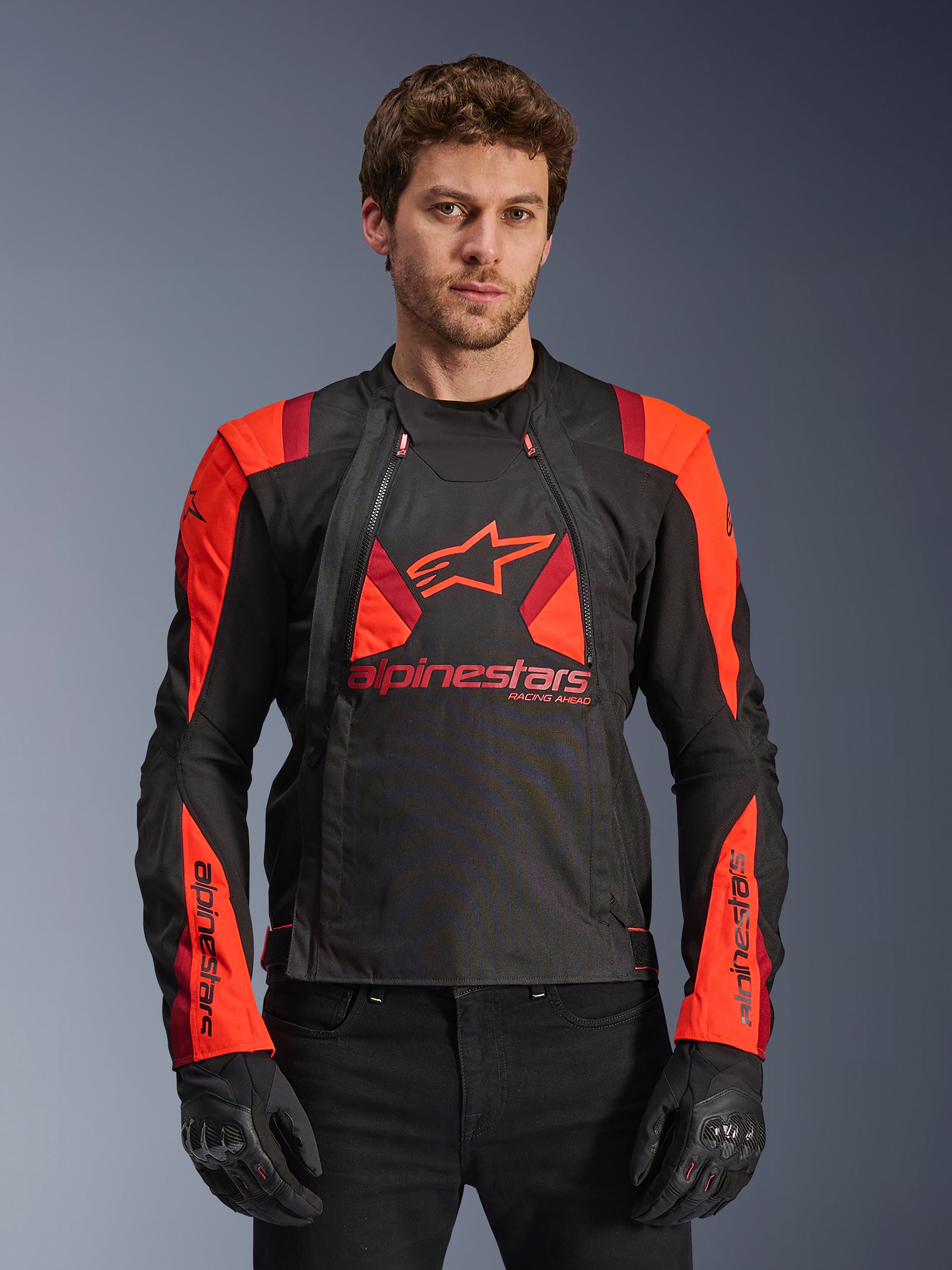 Alpinestars T-Stunt Air Jacket, textiele motorjas, zwart, fluorescerend rood en donkerrood, voorzien van groot sterlogo en mesh-panelen voor ventilatie, gedragen door model met zwarte handschoenen