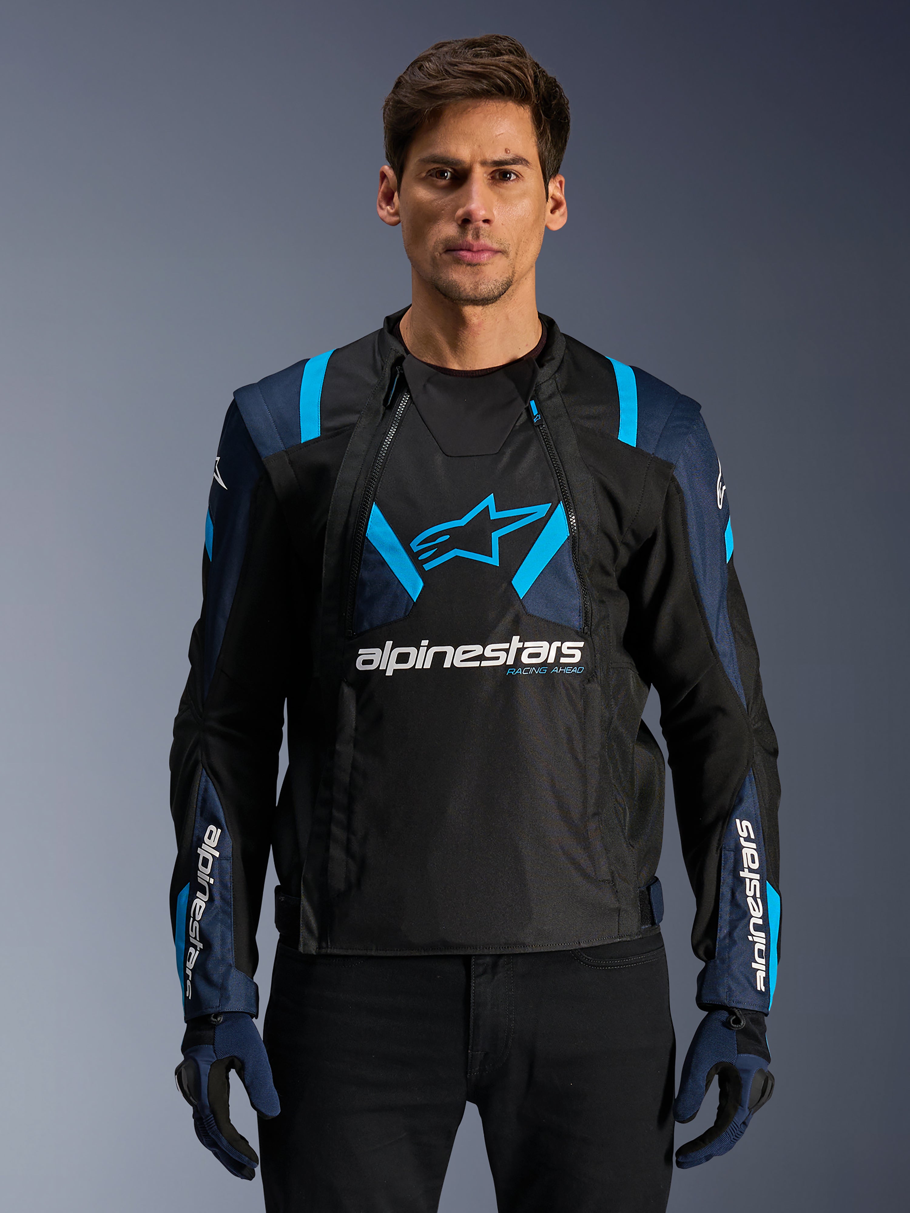 Alpinestars T-Stunt Air Jacket, mesh motorjas, zwart en blauw, gedragen door een model met zwarte broek en handschoenen, voorzien van een modulair 2-in-1 ontwerp met ademende tech-mesh panelen, sterlogo op de borst en Alpinestars-branding op de mouwen.