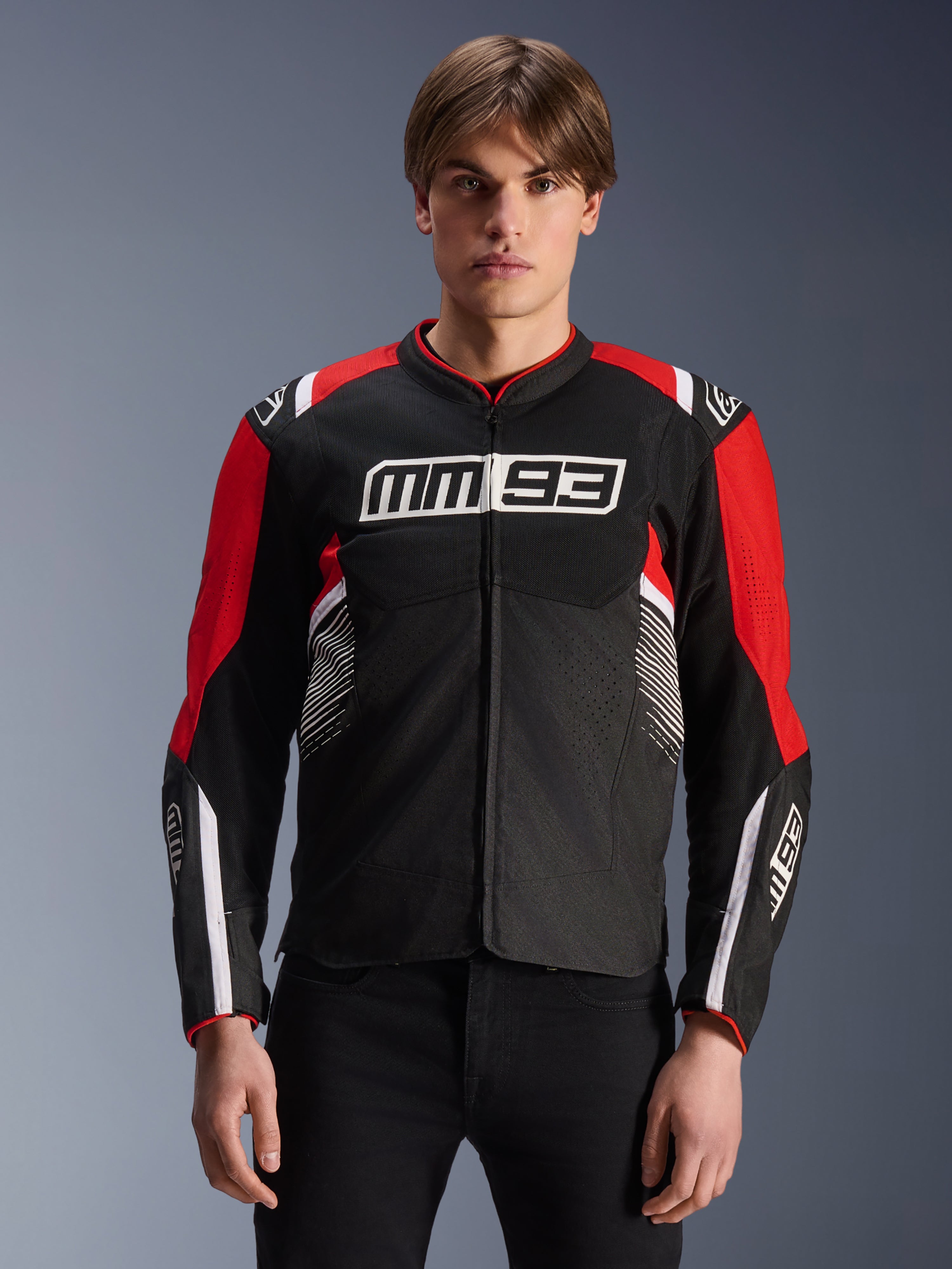 MM93 T-SPS Air V2 Jas, textiele motorjas in zwart, felrood en wit, met Marc Márquez MM93-branding op de borst en mouwen, mesh-panelen voor ventilatie, sportief ontwerp, gedragen door model met zwarte broek
