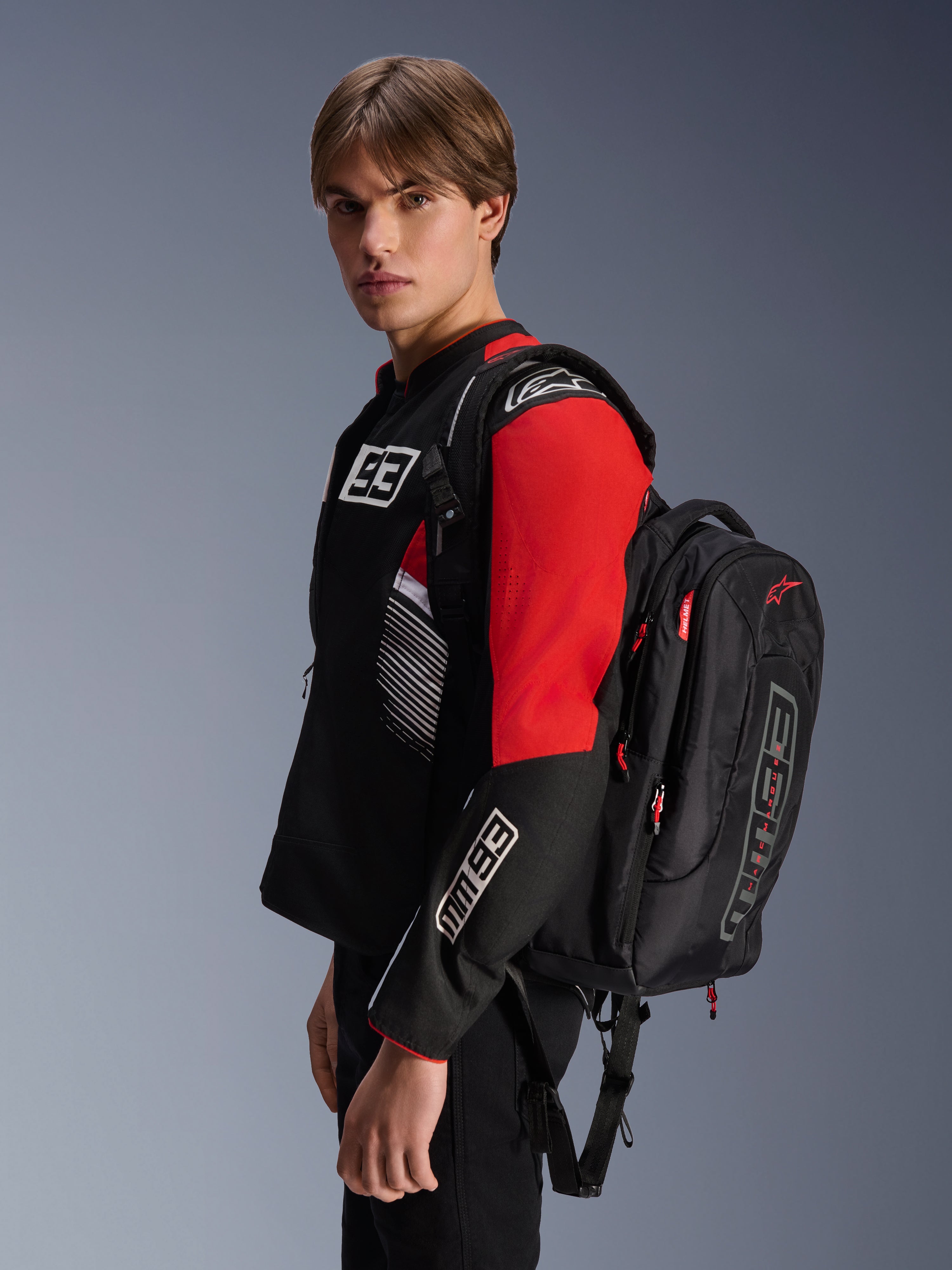 Alpinestars MM93 City Hunter V2 Rugzak, zwart met rode accenten, gedragen door een model in een bijpassende zwarte en rode MM93 motorjas, voorzien van Marc Márquez branding en logo's, urban motorkleding