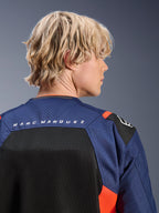 Alpinestars MM93 T-SPS Air V2 Jas, Blue Navy en zwart met Red Fluo accenten, close-up van de bovenrug met 'MARC MARQUEZ' branding, ademende mesh-panelen en geperforeerde textielconstructie, gedragen door een blond model