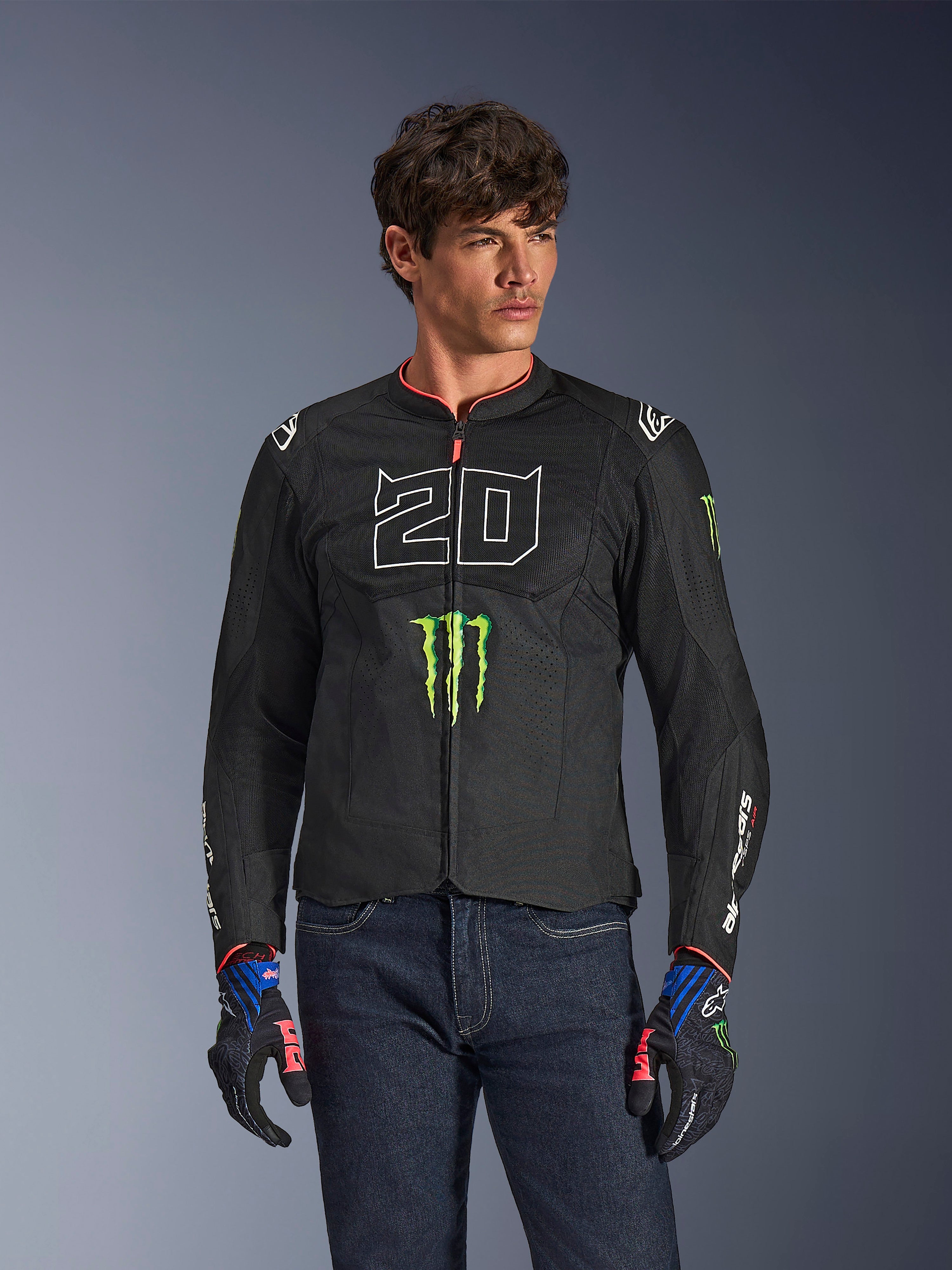 Alpinestars FQ20 T-SPS Air V2 Monster jas, zwarte motorjas met groot wit '20' cijfer en groen Monster Energy-logo, gedragen door een mannelijk model met donkere jeans en bijpassende handschoenen, lichtgewicht mesh-constructie voor stedelijk rijden