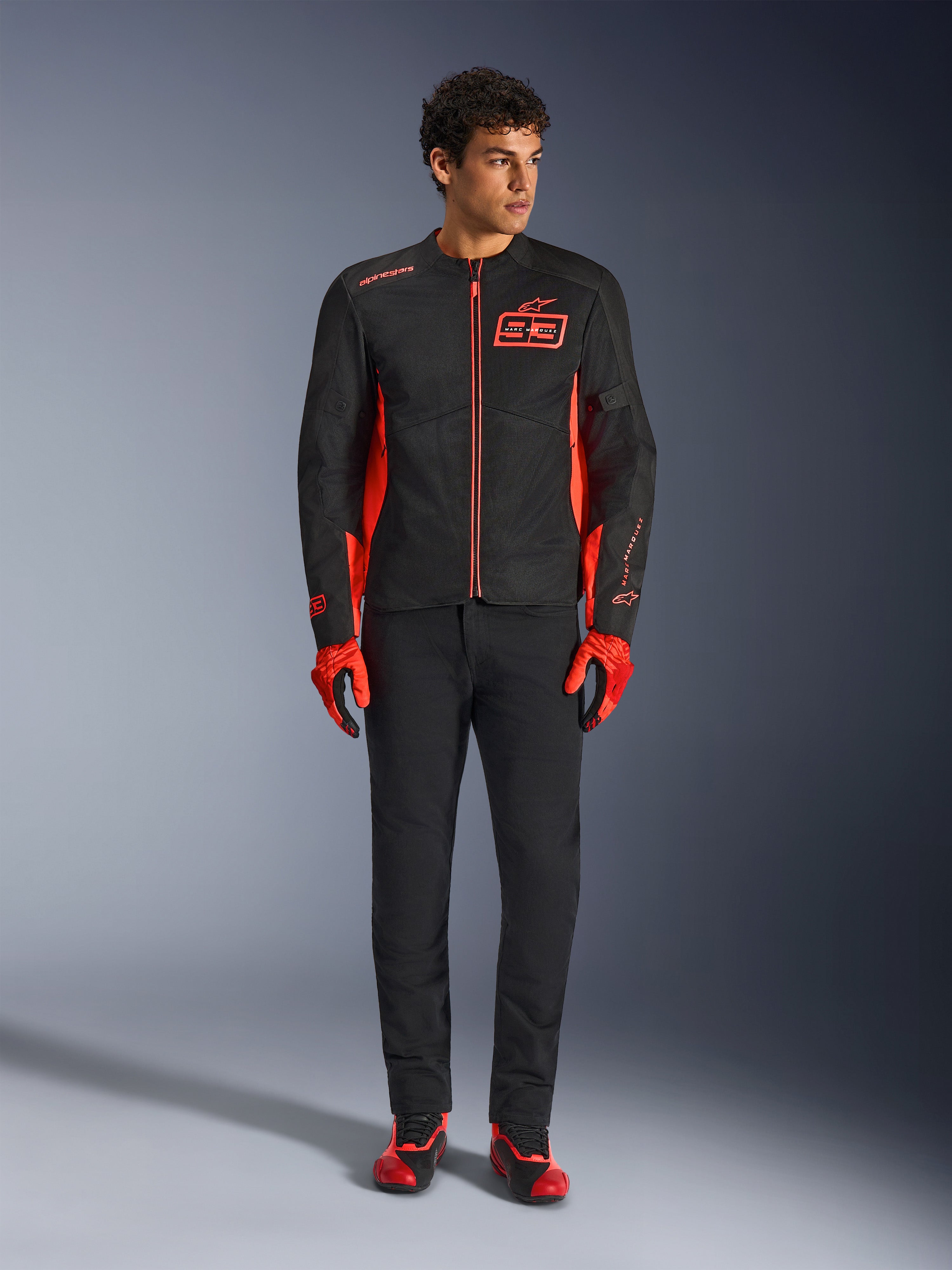 Alpinestars MM93 C-1 Air Jacket, motorjas, zwart en fluo rood, voorzien van Marc Marquez-branding en 93-logo, gedragen door model met bijpassende rode handschoenen en zwarte broek, lichtgewicht textiel- en meshconstructie voor rijden in de stad